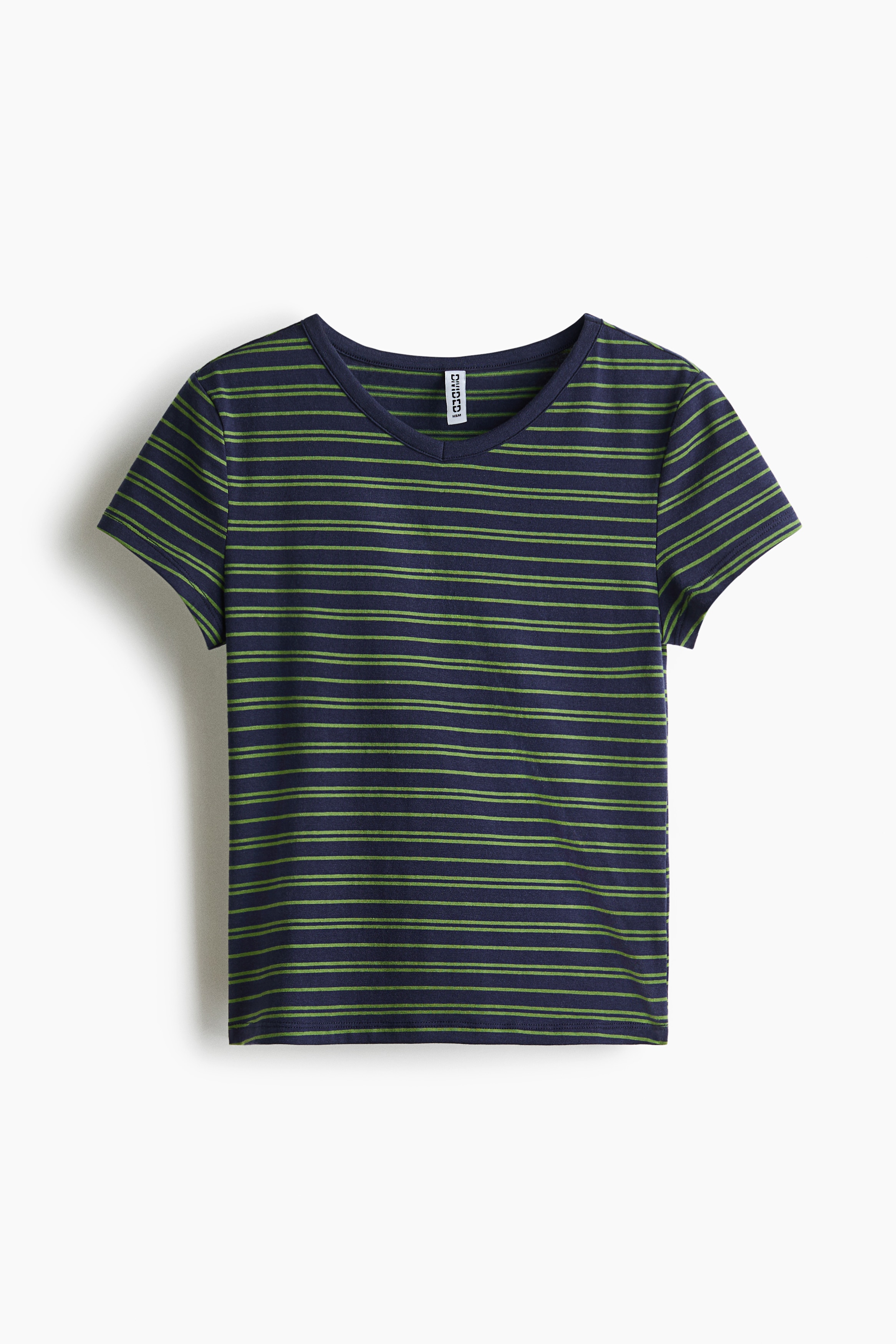La modelo lleva puesta una camiseta de manga corta a rayas, con franjas horizontales en verde y azul marino y cuello redondo. La prenda entallada se combina con jeans de mezclilla clara de tiro bajo y con efecto desgastado.