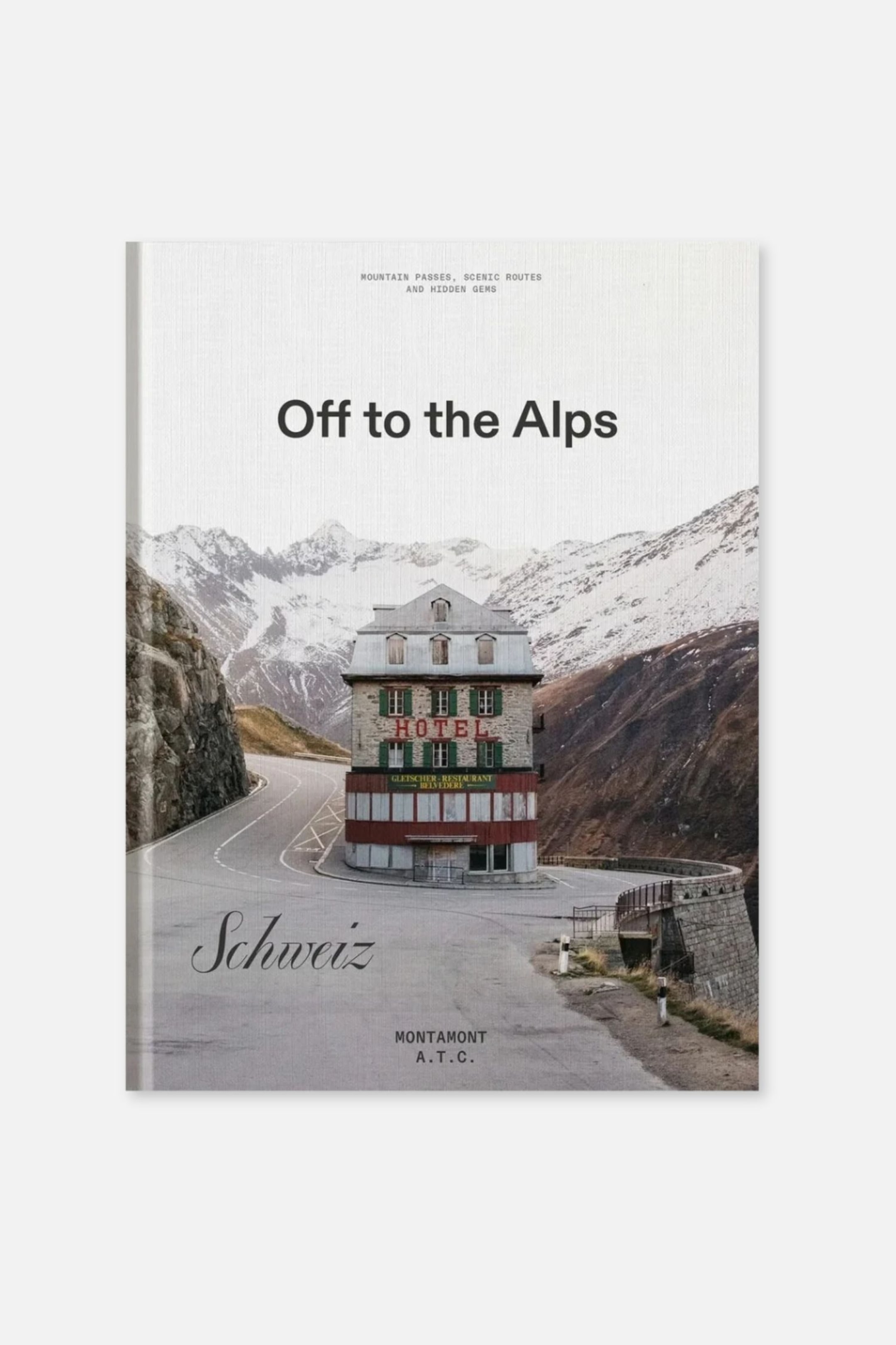 Ver imagen más grande: Una vista frontal muestra el libro titulado «Off to the Alps», que presenta una fotografía de portada panorámica de un hotel de varias plantas situado en una sinuosa carretera de montaña rodeada de cumbres nevadas. En la portada aparece el título principal en negrita negra cerca de la parte superior, con la palabra «Schweiz» escrita en letra cursiva en la parte inferior izquierda y «MONTAMONT A.T.C.» impreso en el centro inferior.