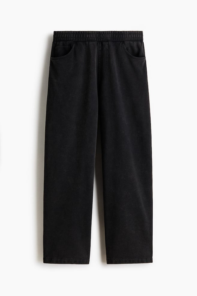 Black sweatpants shown from the front, featuring an elasticated waistband, two curved side pockets and a wide-leg design, all in a slightly faded black colour with a plain hem. - 1