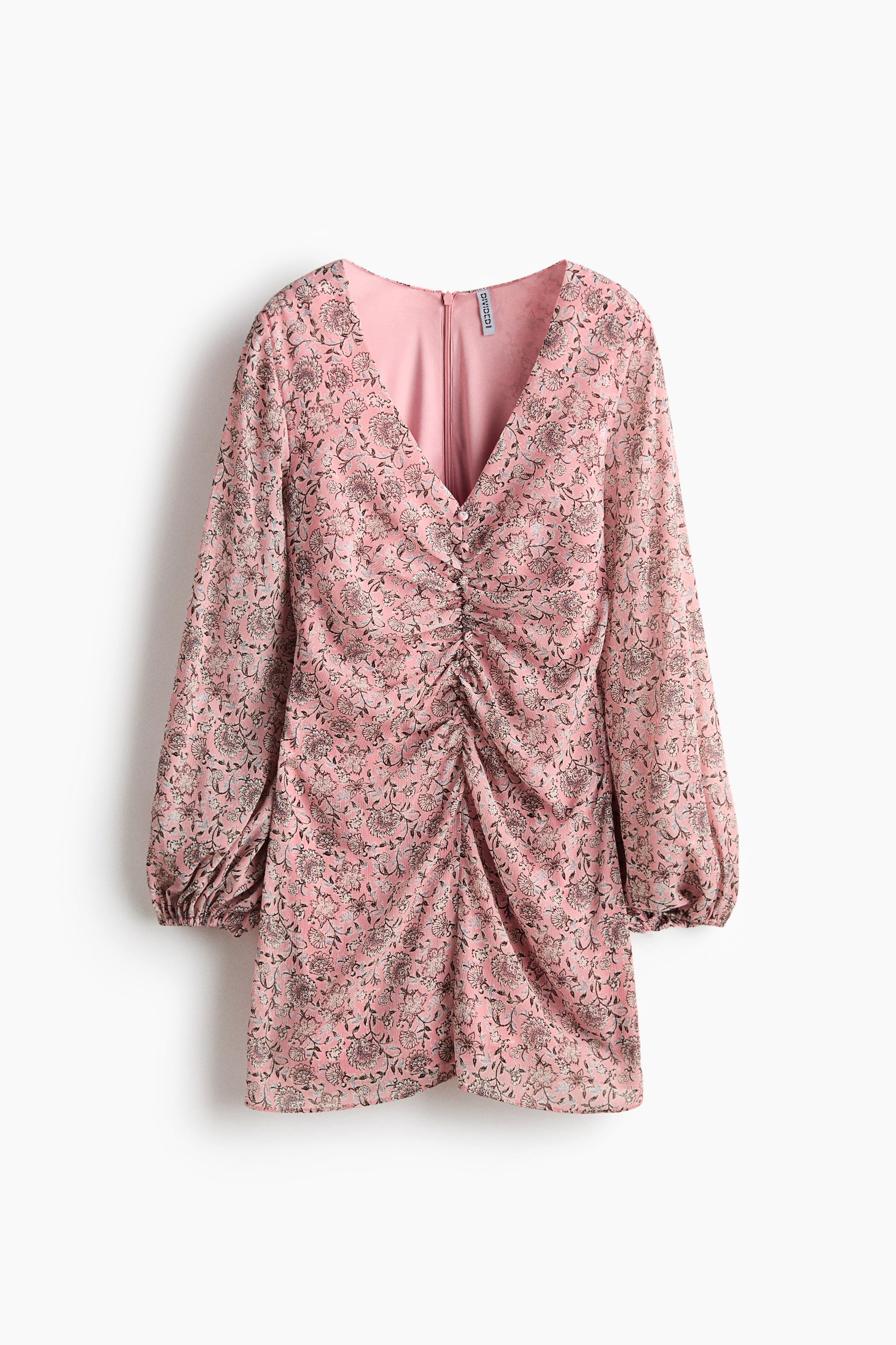 הצגת תמונה גדולה יותר: שמלה פרחונית ורודה מוצגת מלפנים, עם מחשוף בצורת V ושרוולי בלון ארוכים עם סיומות אלסטיות. החלק העליון מציג רושינג מרכזי המאובטח על-ידי כפתורים קטנים דקורטיביים, והבד מכוסה בדוגמת פרחים כהה.