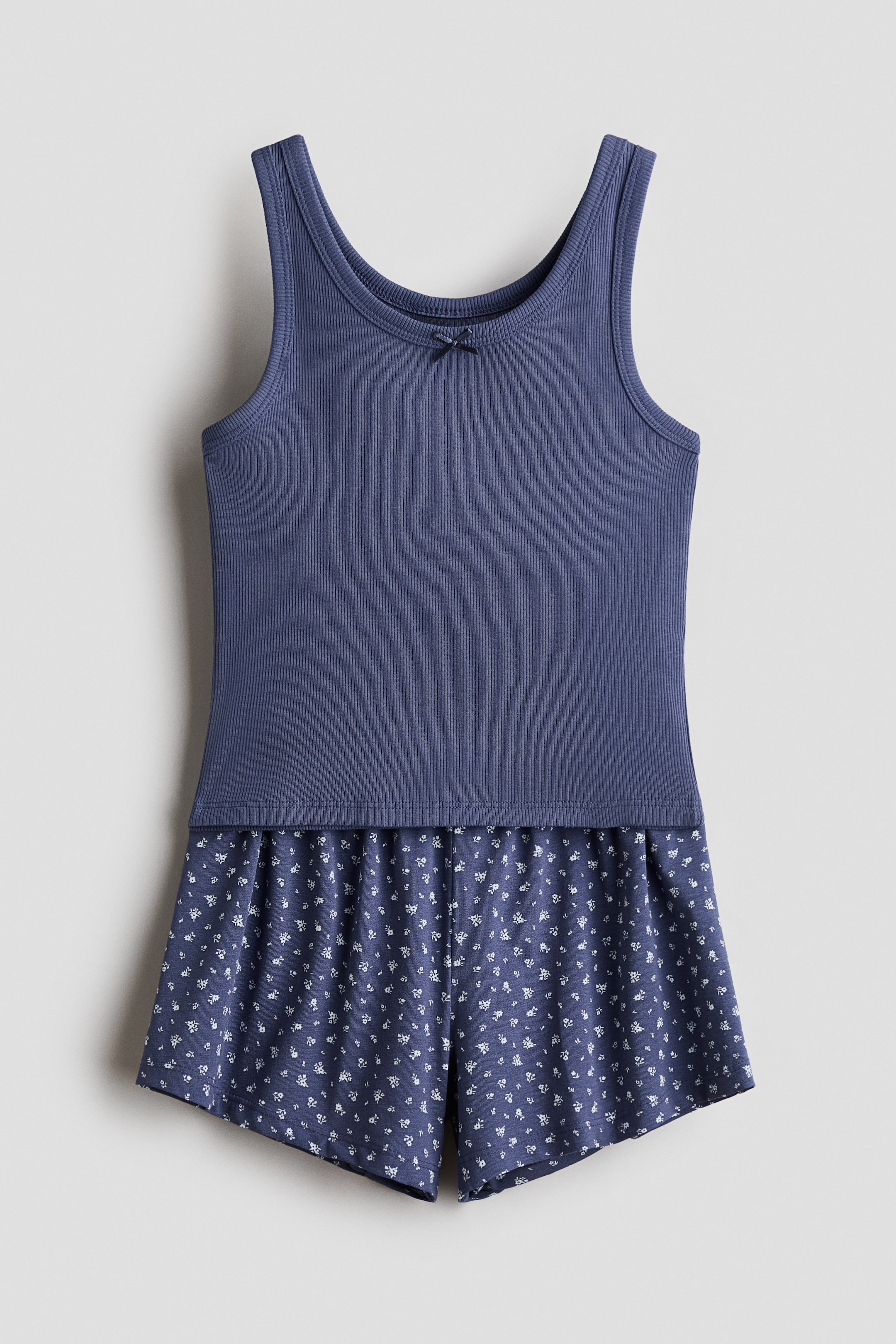 View larger image: A pyjamas set features a dark blue ribbed vest top with a scoop neckline, binding around the neckline and armholes, and a small decorative satin bow at the centre front. The matching shorts are patterned with small white flowers on a dark blue background and feature an elasticated waist.