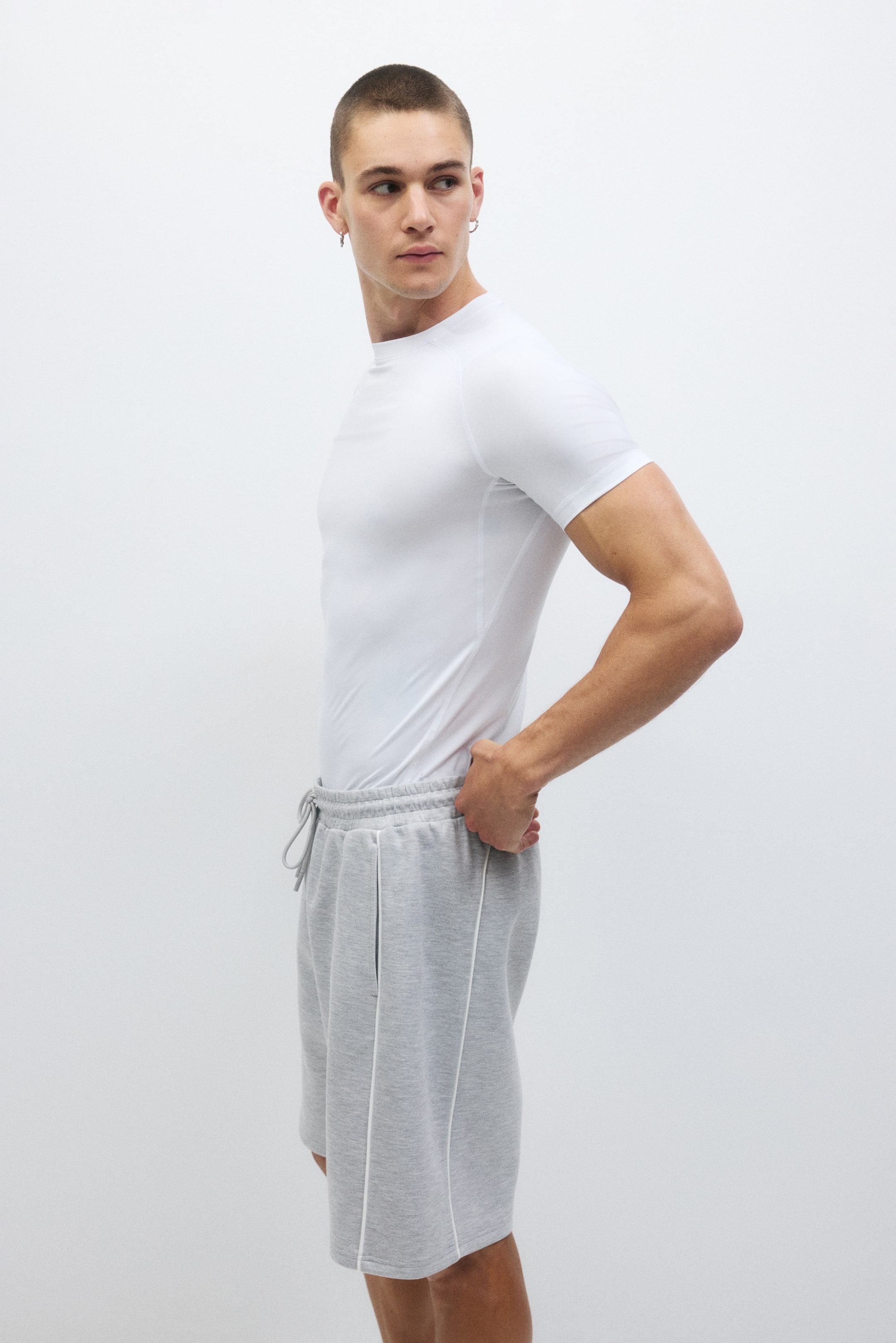 View larger image: Gray marl knit shorts feature an elastic waistband with a visible drawstring, complemented by side seam pockets with white piping running vertically along them and down the side seams, offering a relaxed fit from a side view.