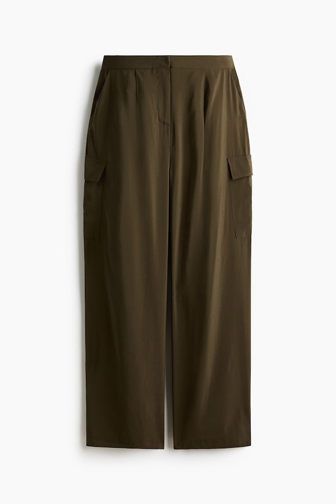 Dark olive green pants are showcased in a front view, featuring a flat waistband, a central front seam, subtle pleats, and flap cargo pockets on each wide leg. - 1