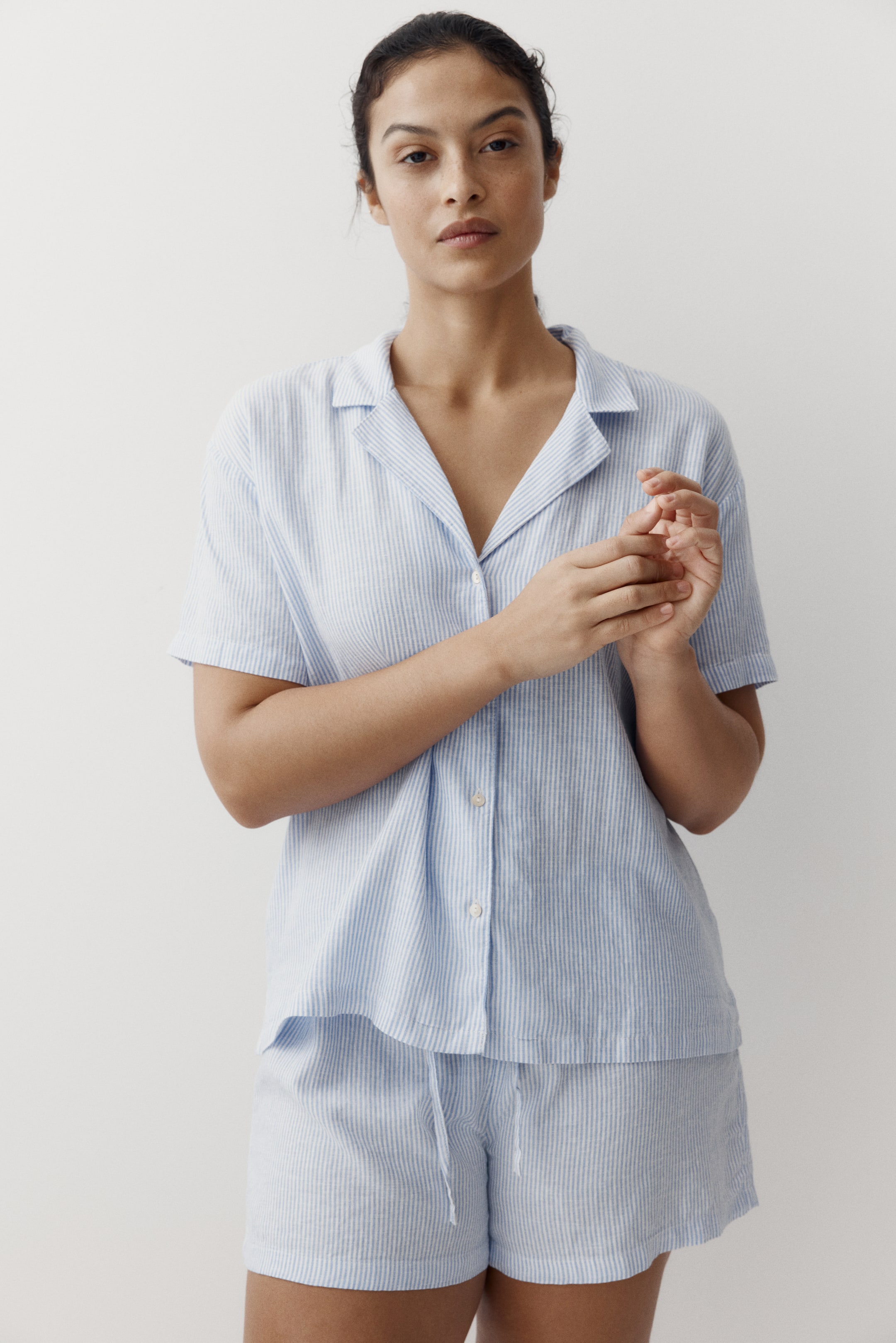 View larger image: The light blue and white vertical striped pyjama set is showcased front-facing, comprising a short-sleeved top and matching shorts. The top features a button-front closure and a relaxed collar, while the shorts boast a drawstring waist.