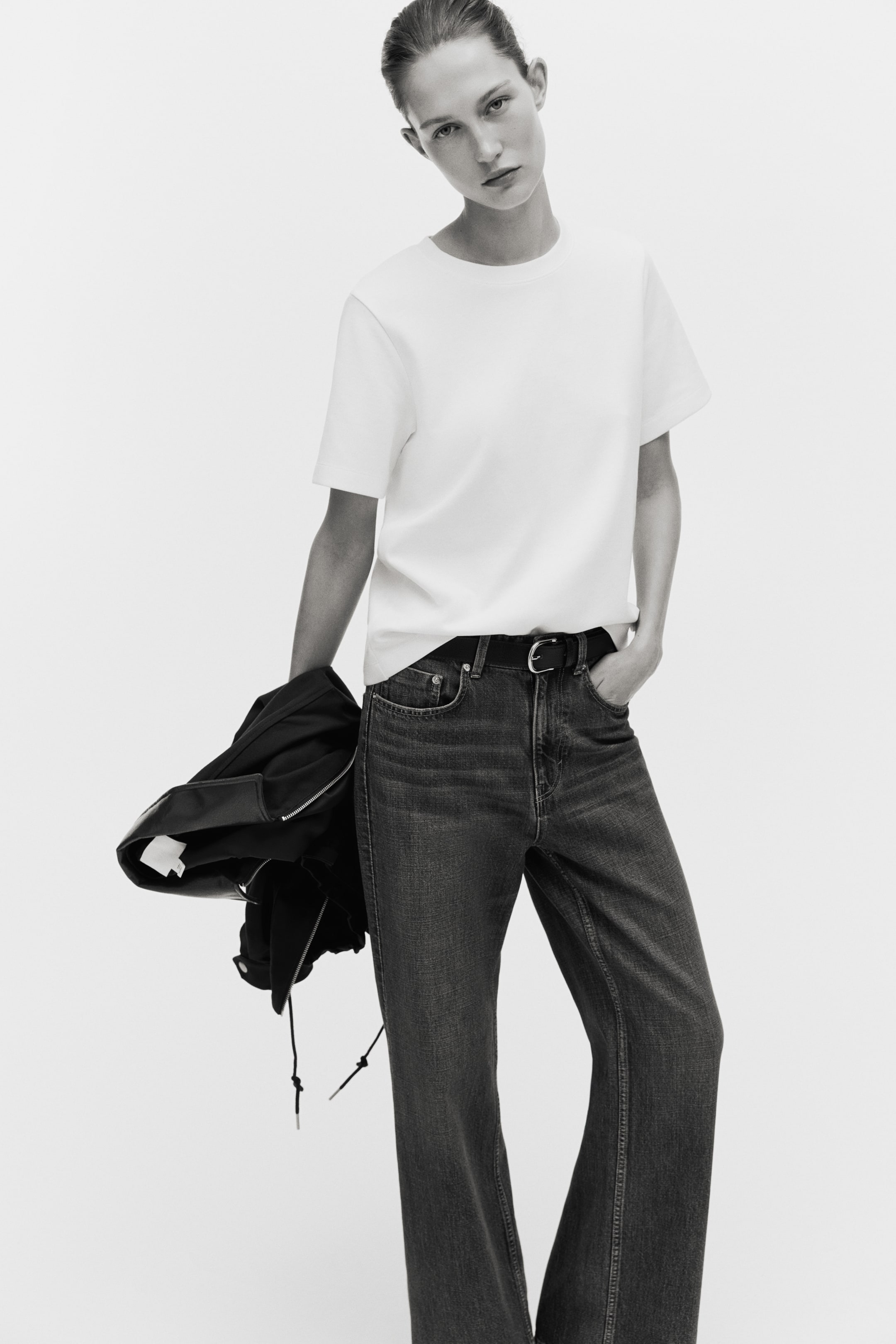 View larger image: A white crew-neck T-shirt is styled partially tucked into dark-wash, high-waisted, straight-leg jeans. A black belt with a silver-toned buckle secures the jeans.
