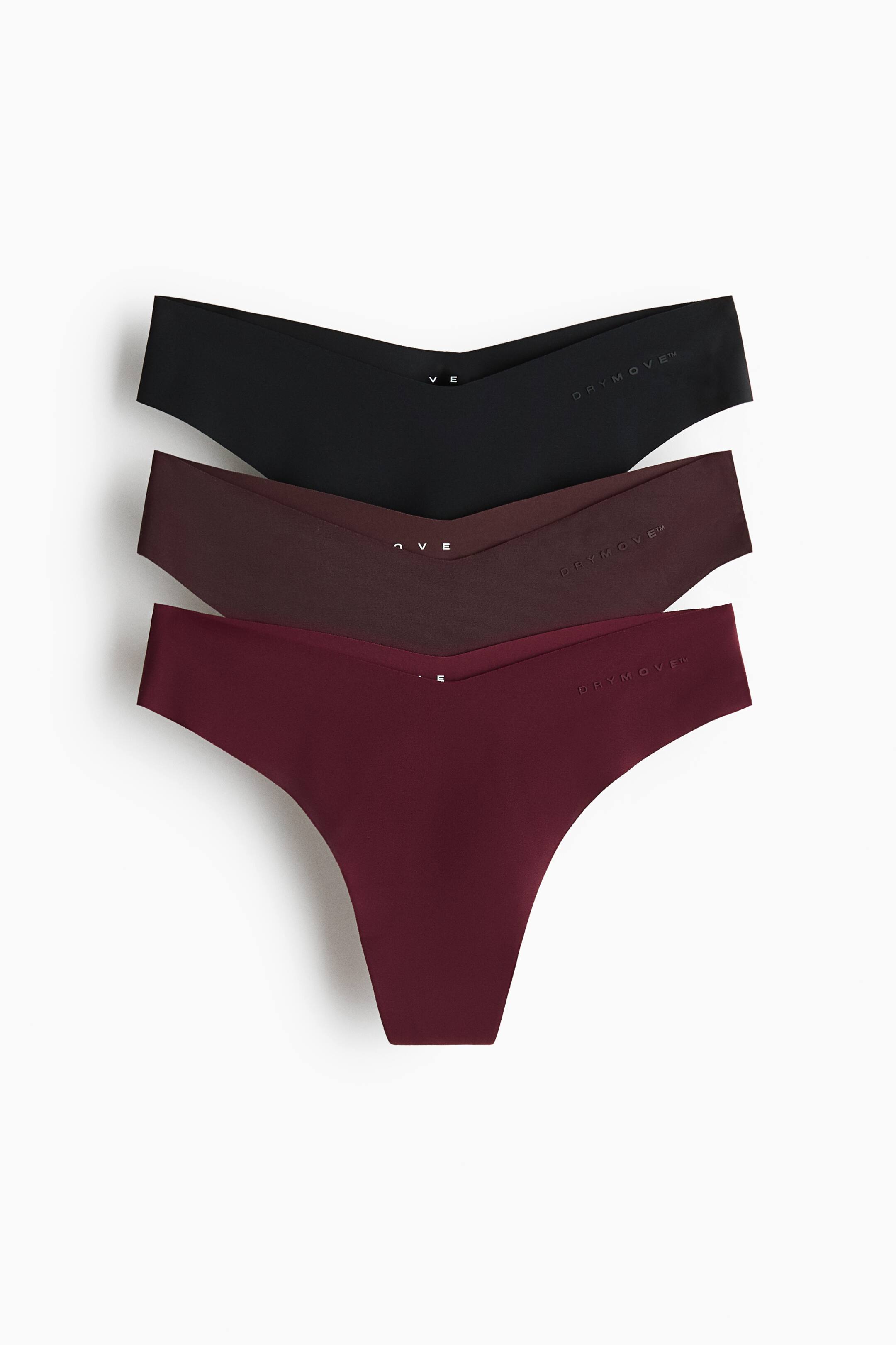Visa större bild: Ett 3-pack sportstringtrosor ligger plant och något vinklat, vilket visar deras V-formade midjeband framtill. Stringtrosorna är staplade, med en svart överst, en mörk plommonfärgad i mitten och en vinröd längst ner, alla subtilt präglade med 'DRYMOVE?' på midjebandet.