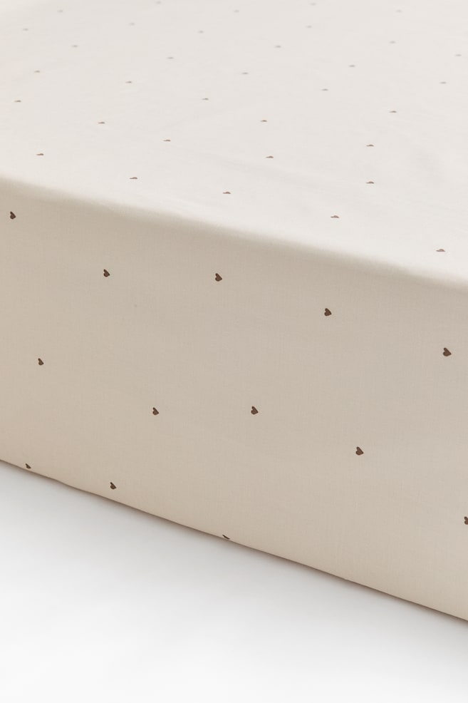 Un drap-housse en coton tissÃ© Ã©cru clair, ornÃ© dâun motif de petits cÅurs bruns Ã©parpillÃ©s, enveloppe parfaitement le coin dâun matelas. La vue rapprochÃ©e en angle met en valeur lâajustement lisse et la finition nette du drap. - 1