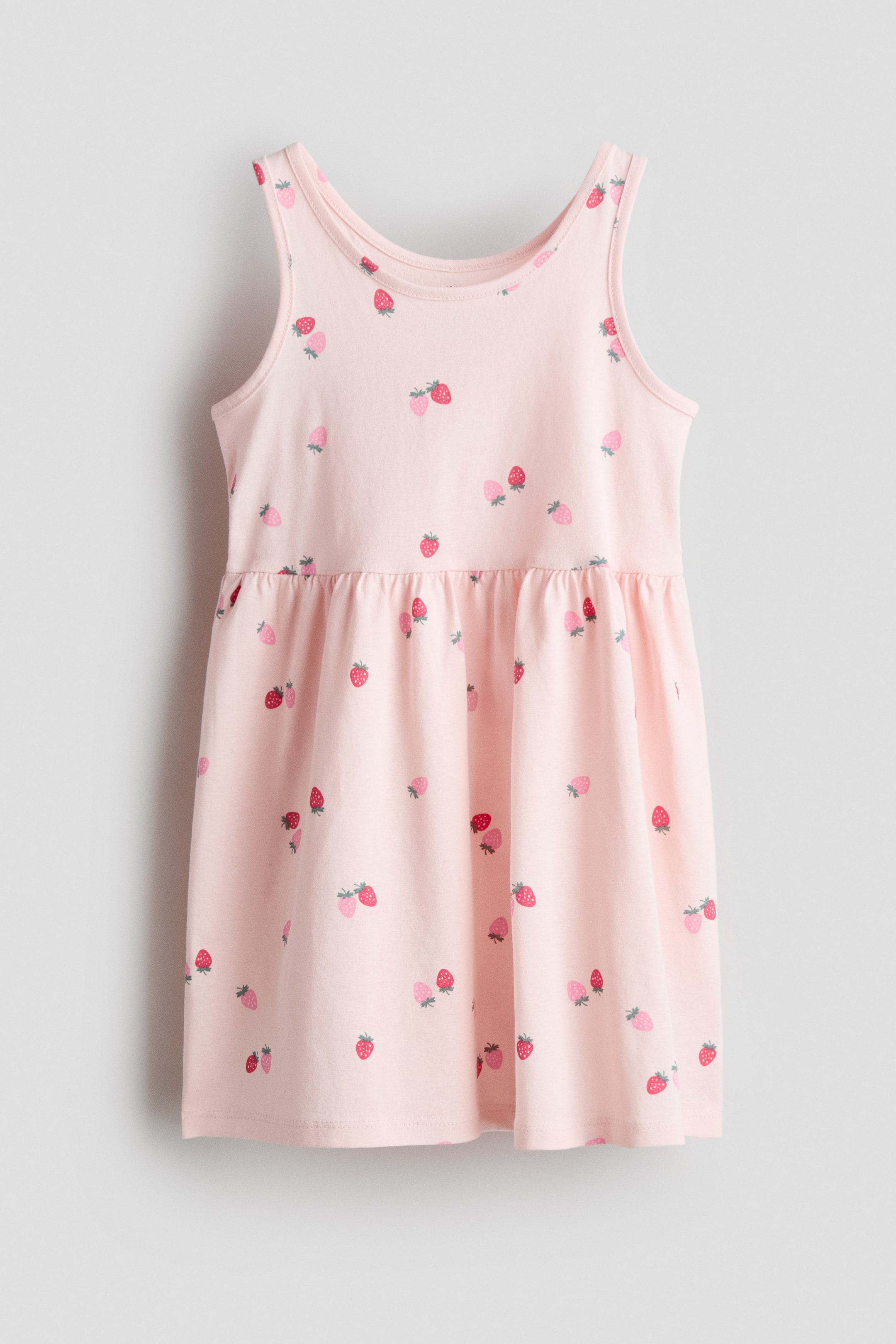 View larger image: A comfortable sleeveless dress in soft, patterned cotton jersey is shown from the front. It features a pink base color with an all-over strawberry pattern, a gathered seam at the waist, and a gently flared skirt.