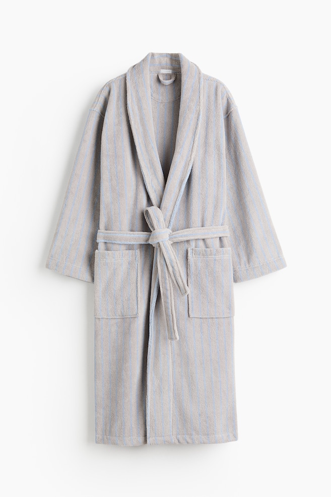 A striped dressing gown is presenting front, featuring a shawl collar and two front patch pockets. A detachable tie belt is knotted at the waist, cinching the light brown terry fabric with light blue stripes. - 1
