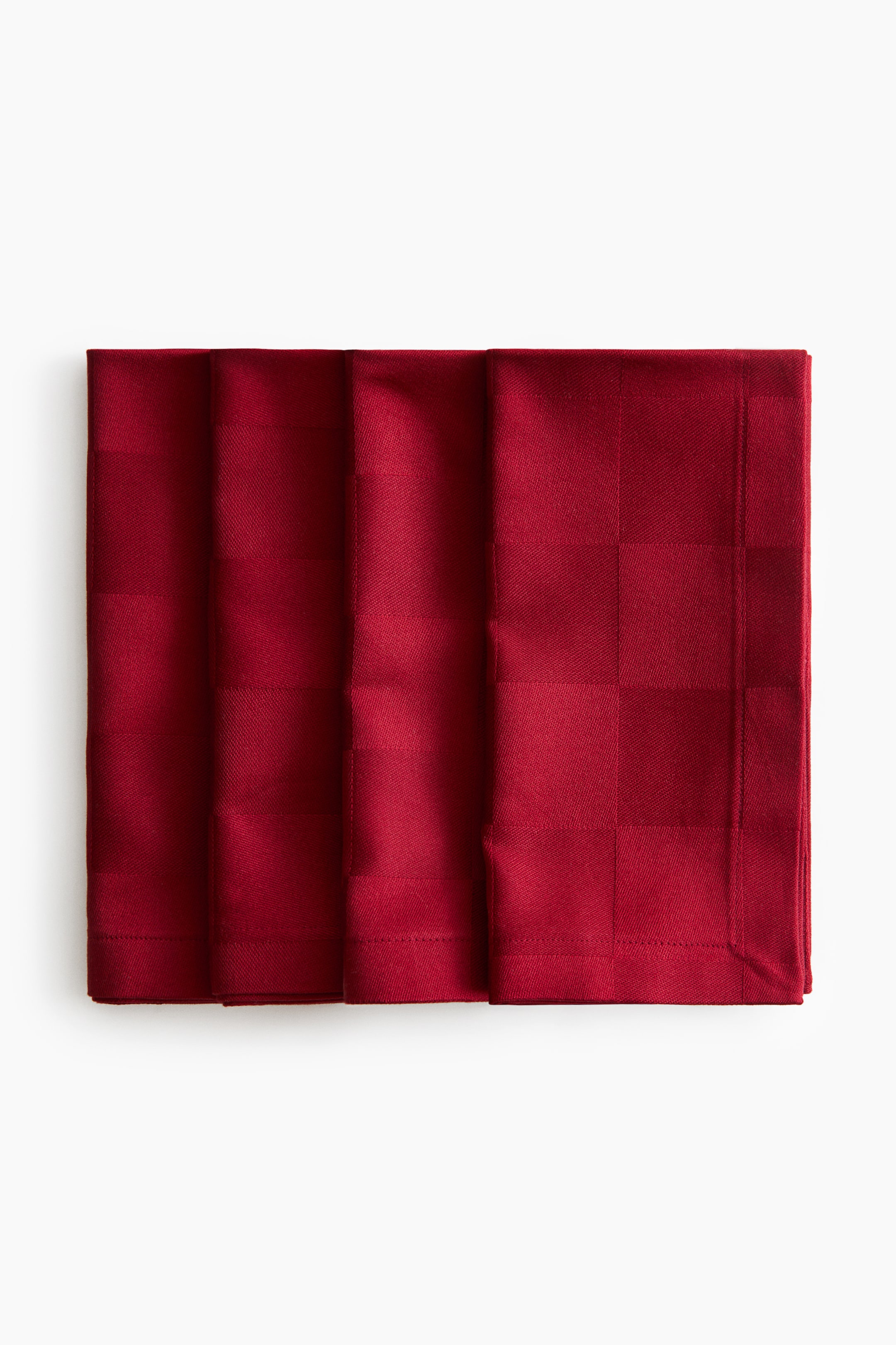 Ver imagen más grande: Un conjunto de cuatro servilletas de tela rojas está dispuesto en una fila ligeramente superpuesta, orientadas hacia el frente, mostrando un sutil patrón de cuadro tejido. Las servilletas dobladas exhiben dobladillos cosidos en los bordes.