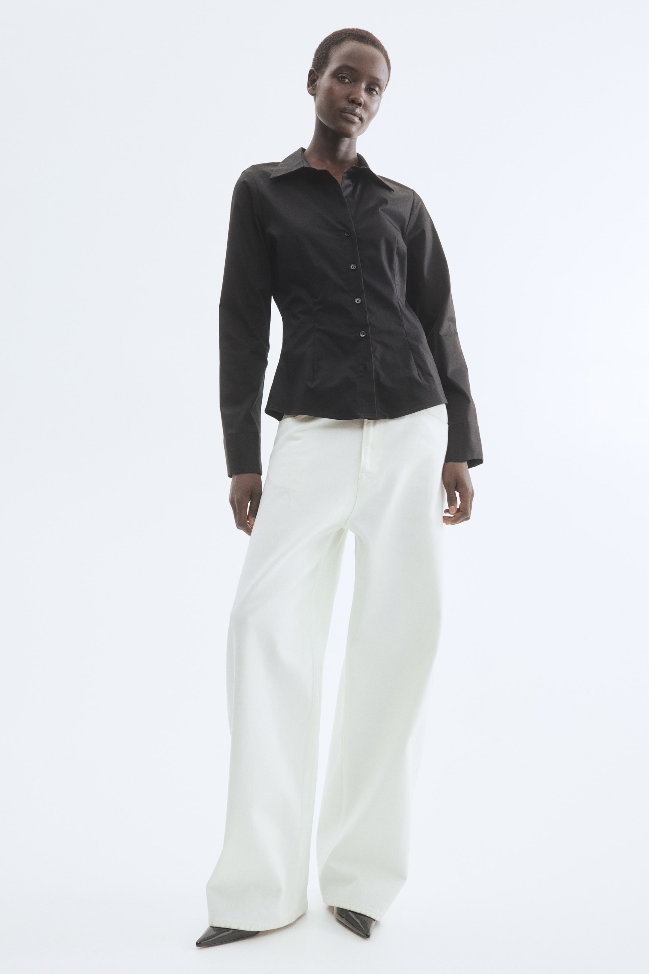 הצגת תמונה גדולה יותר: חולצה שחורה עם כפתורים, בעלת צווארון מחודד, שרוולים ארוכים עם חפתים מכופתרות, וחזית עם שישה כפתורים נראים. החולצה מציגה גזרה מחויטת, המתחדדת במותניים.