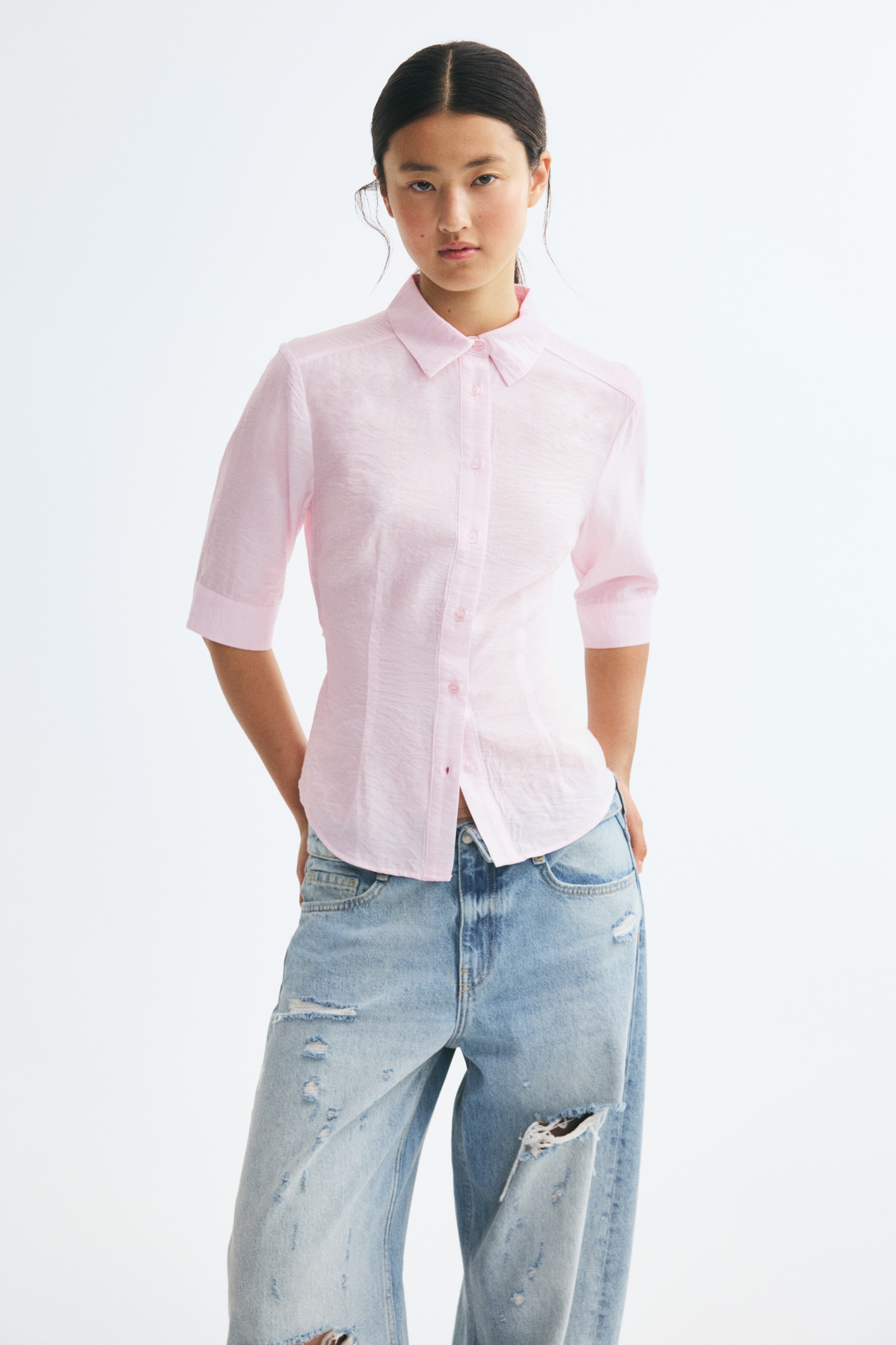 A light pink button-down shirt is shown from the front, featuring a classic point collar, a button placket, and elbow-length sleeves with wide cuffs. The shirt has a slightly textured finish and vertical darts that provide a tailored fit.