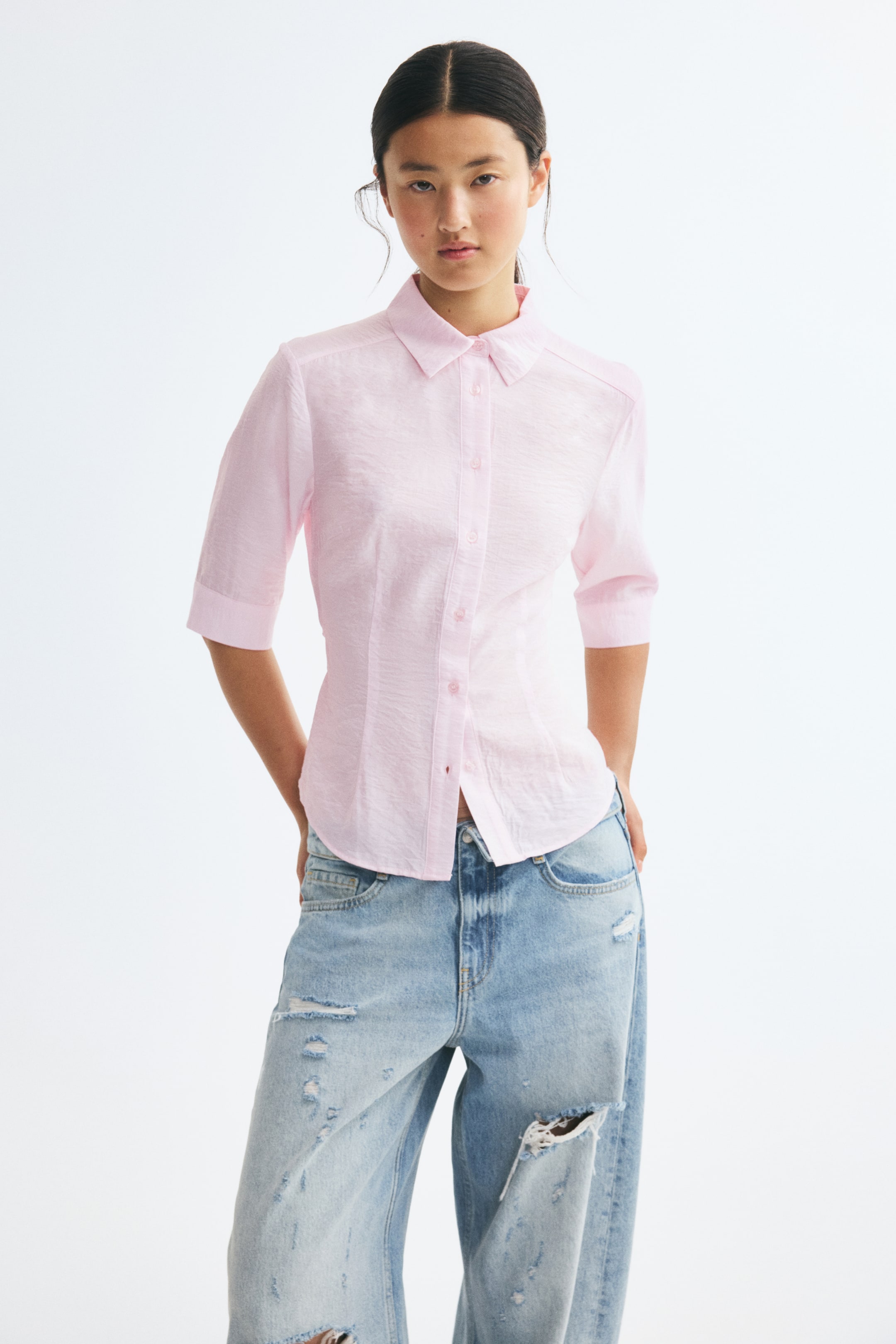 View larger image: A light pink, textured-weave fitted shirt is shown from the front, featuring a pointed collar, a button-down front, and 3/4-length sleeves. The shirt highlights a tailored silhouette with shaping waist darts at the front and a rounded hem.
