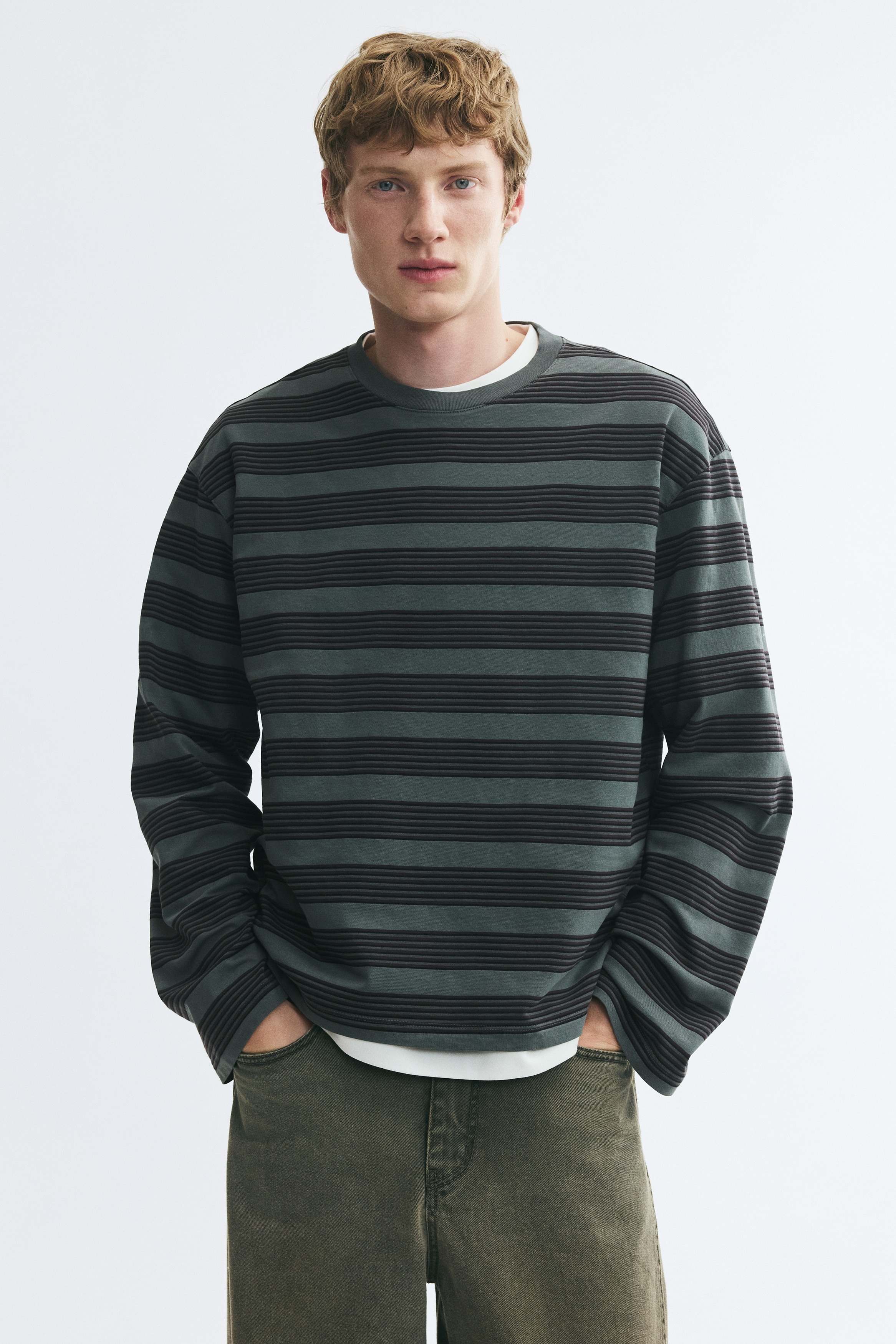 Una t-shirt boxy a maniche lunghe con righe orizzontali verde scuro e nere Ã¨ appesa ÑÑÐ¾Ð½ÑÐ°Ð»mente. Mostra una silhouette rilassata con scollo rotondo a coste, spalle scese e orlo dritto.