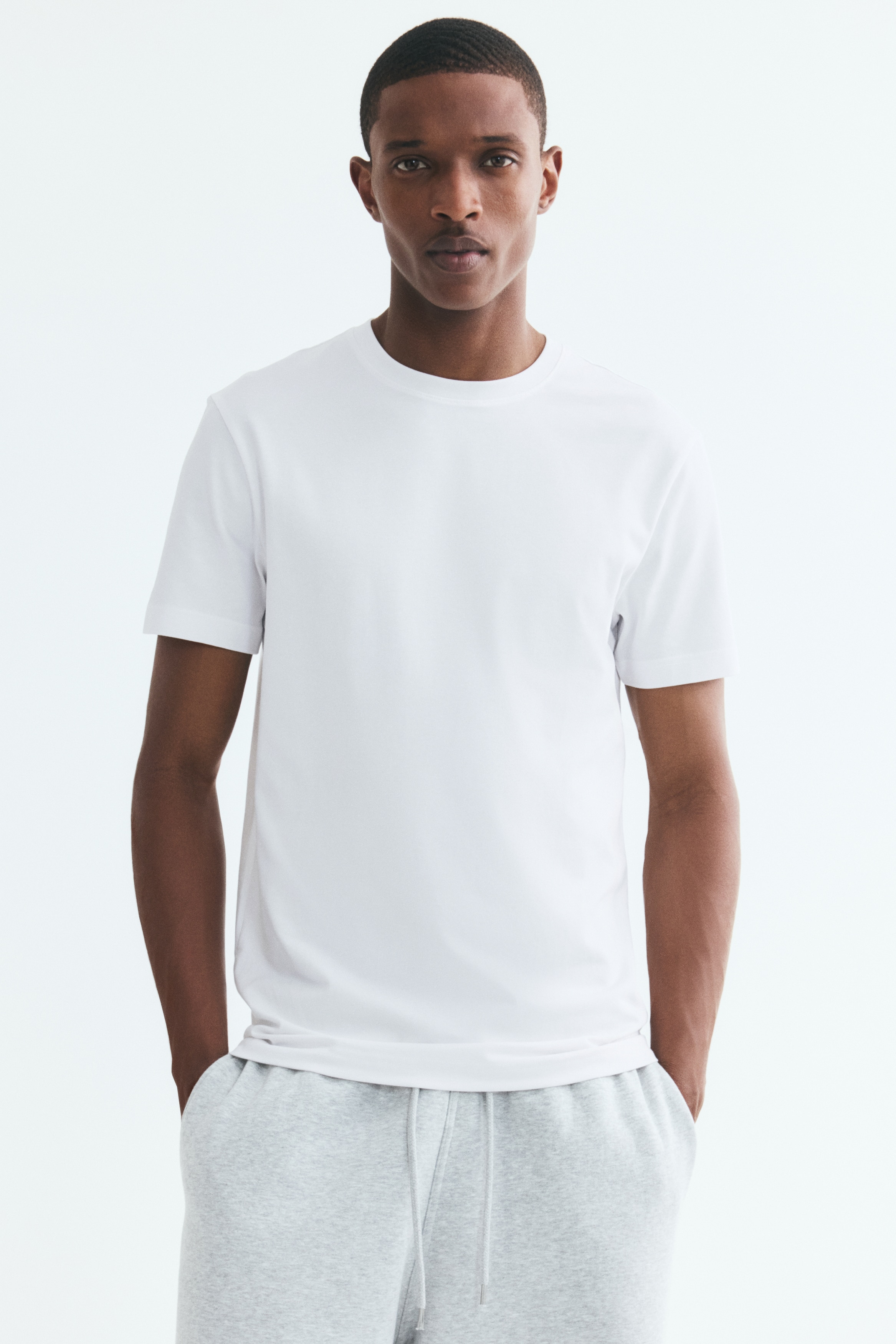A white T-shirt is laid flat and facing forward, featuring a crew neck and short sleeves. A black brand tag is visible inside the back of the neck.