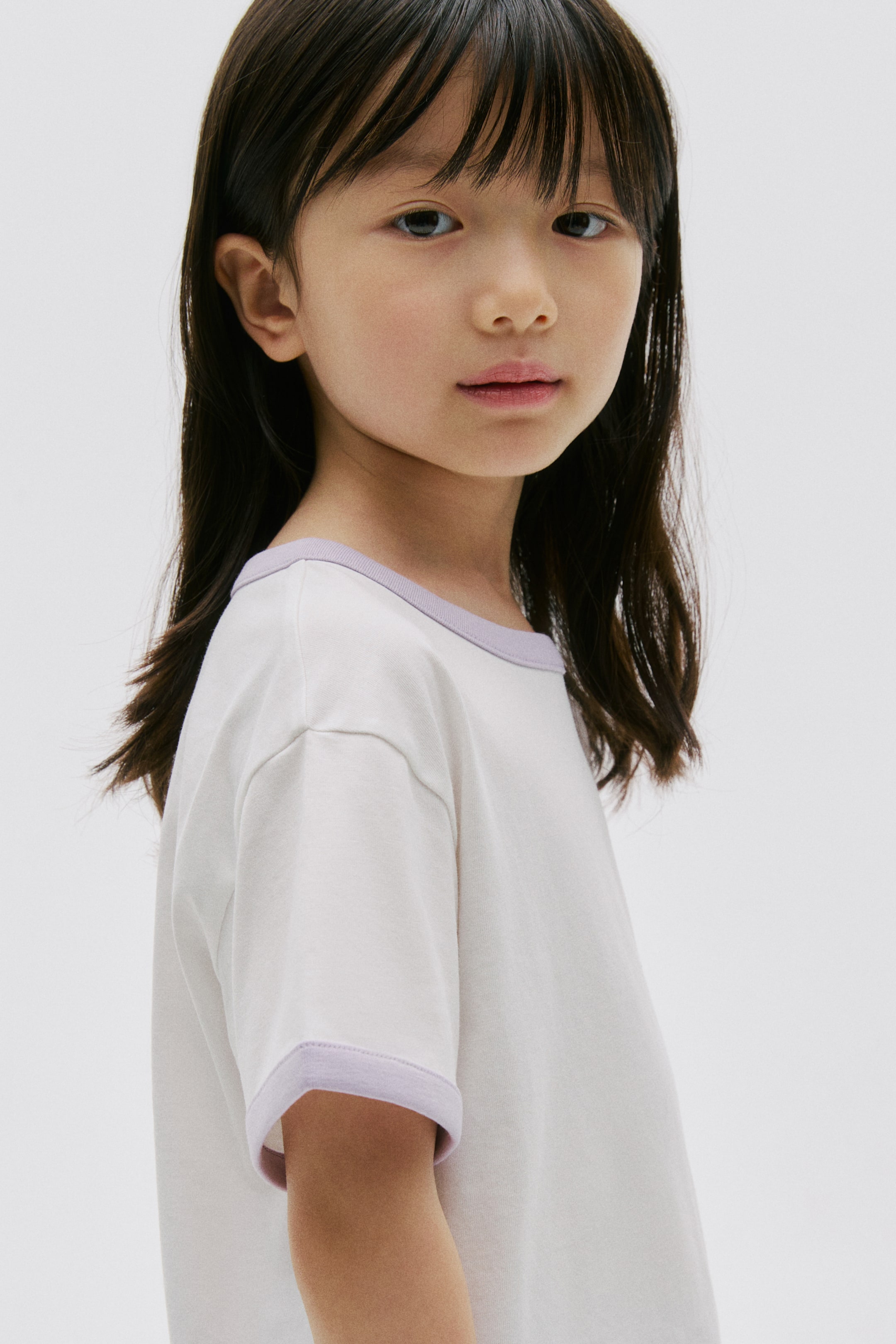 View larger image: The t-shirt is featuring an off-white body with a round neckline and short sleeves. It is detailed with a contrasting light purple trim along the neckline and sleeve cuffs, presenting a slight side view.