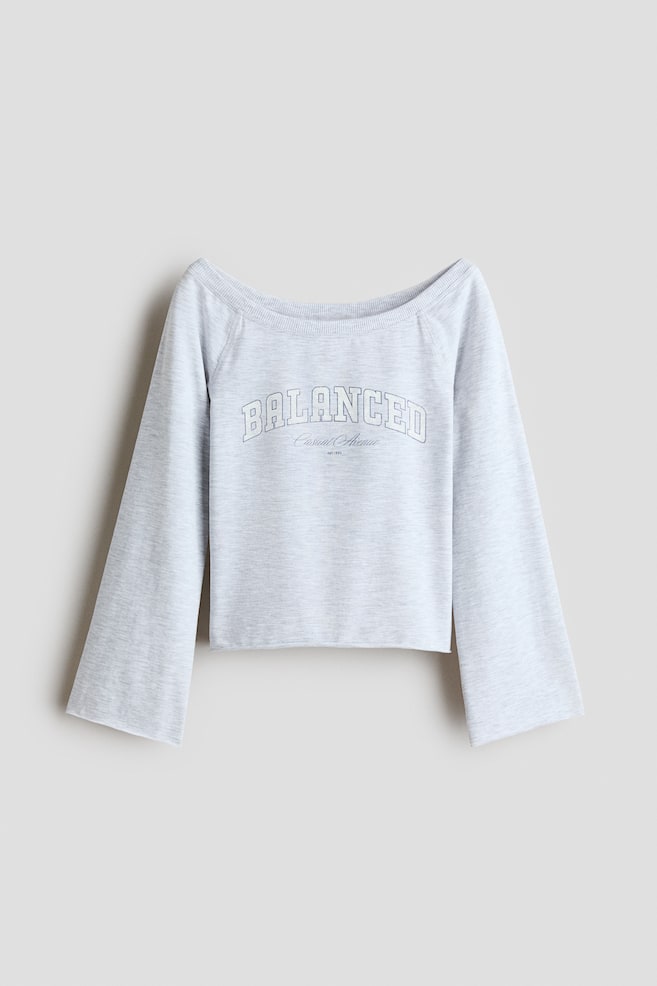 Se muestra una sudadera de mezcla gris claro, vista de frente, con un amplio escote barco ribeteado de canalé y mangas raglán largas y anchas. En el pecho presenta un estampado tipográfico con borde blanco que dice âBALANCEDâ sobre una inscripción más pequeña, con bordes en bruto rematados en dobladillo enrollado en los puños y el bajo. - 1