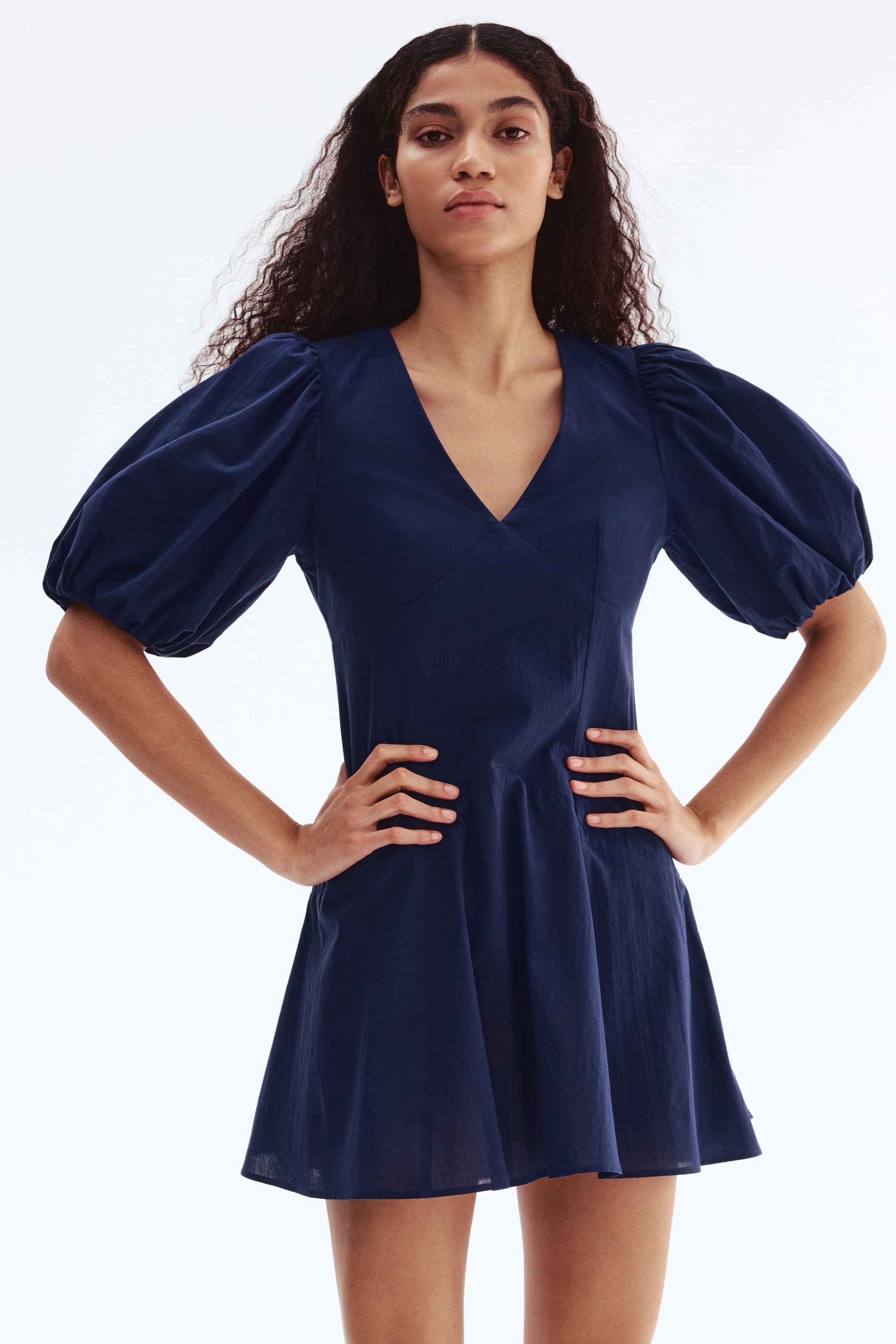 Ampliar la imagen: Un vestido mini azul oscuro presenta un escote en V profundo y mangas abullonadas hasta el codo, recogidas en los hombros y los puños. El vestido cuenta con un corpiño ajustado, ceñido en la cintura, y se despliega en una falda mini acampanada.