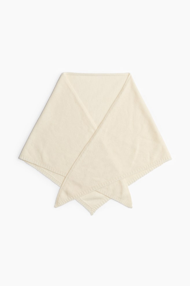 Un paÃ±uelo triangular de color crema estÃ¡ extendido, mostrando su textura suave de punto fino y sus bordes acanalados. El paÃ±uelo estÃ¡ doblado en la parte delantera, con los extremos puntiagudos superpuestos para mostrar su forma. - 1