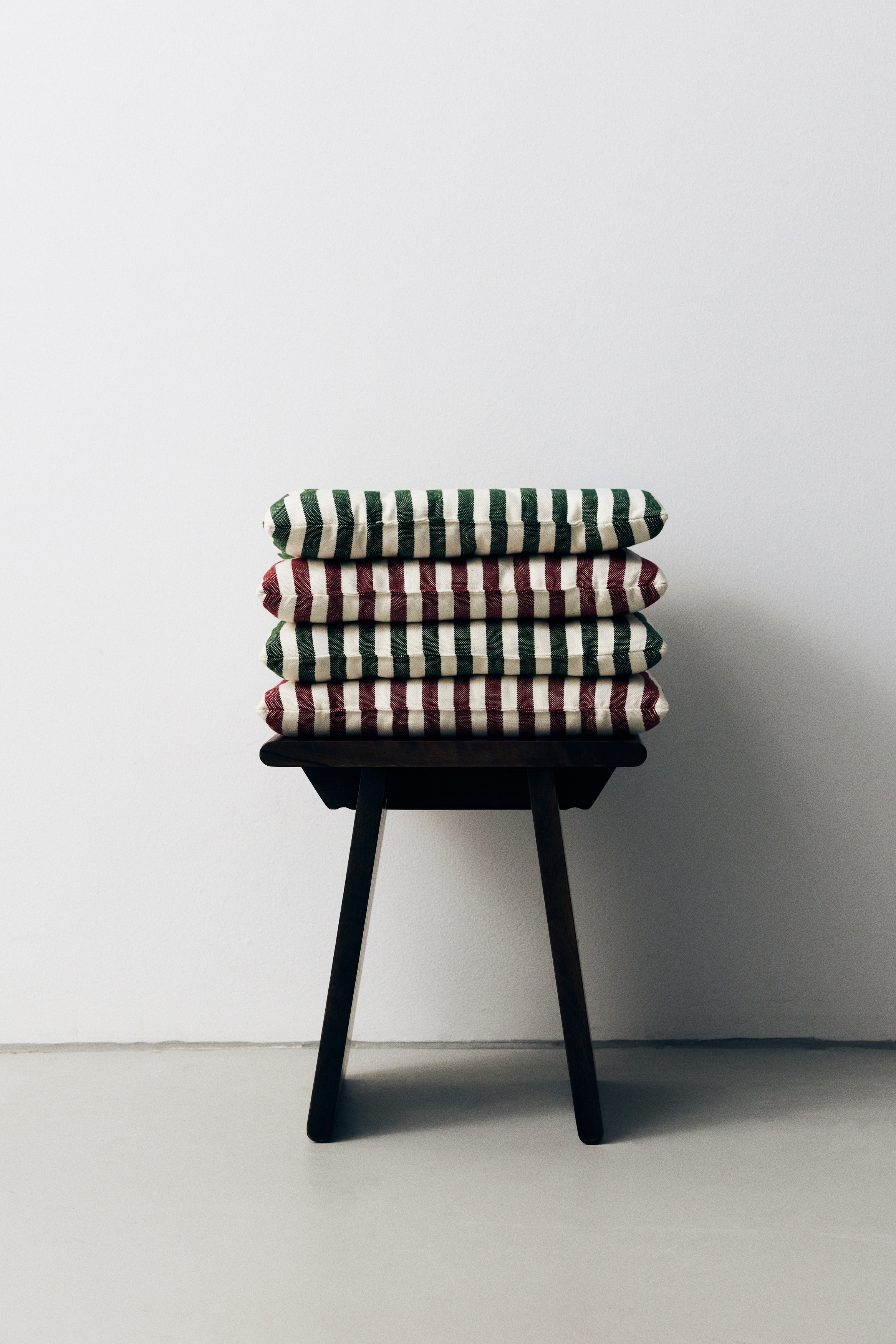 Zwei quadratische gepolsterte Sitzkissen sind in der Draufsicht zu sehen und zeigen ein vertikales gestreiftes Muster in DunkelgrÃ¼n und Off-White. Beide Kissen verfÃ¼gen Ã¼ber ein gestepptes Design mit in einem Raster Ã¼ber die OberflÃ¤che angeordneten, mit KnÃ¶pfen versehenen Quiltknoten.