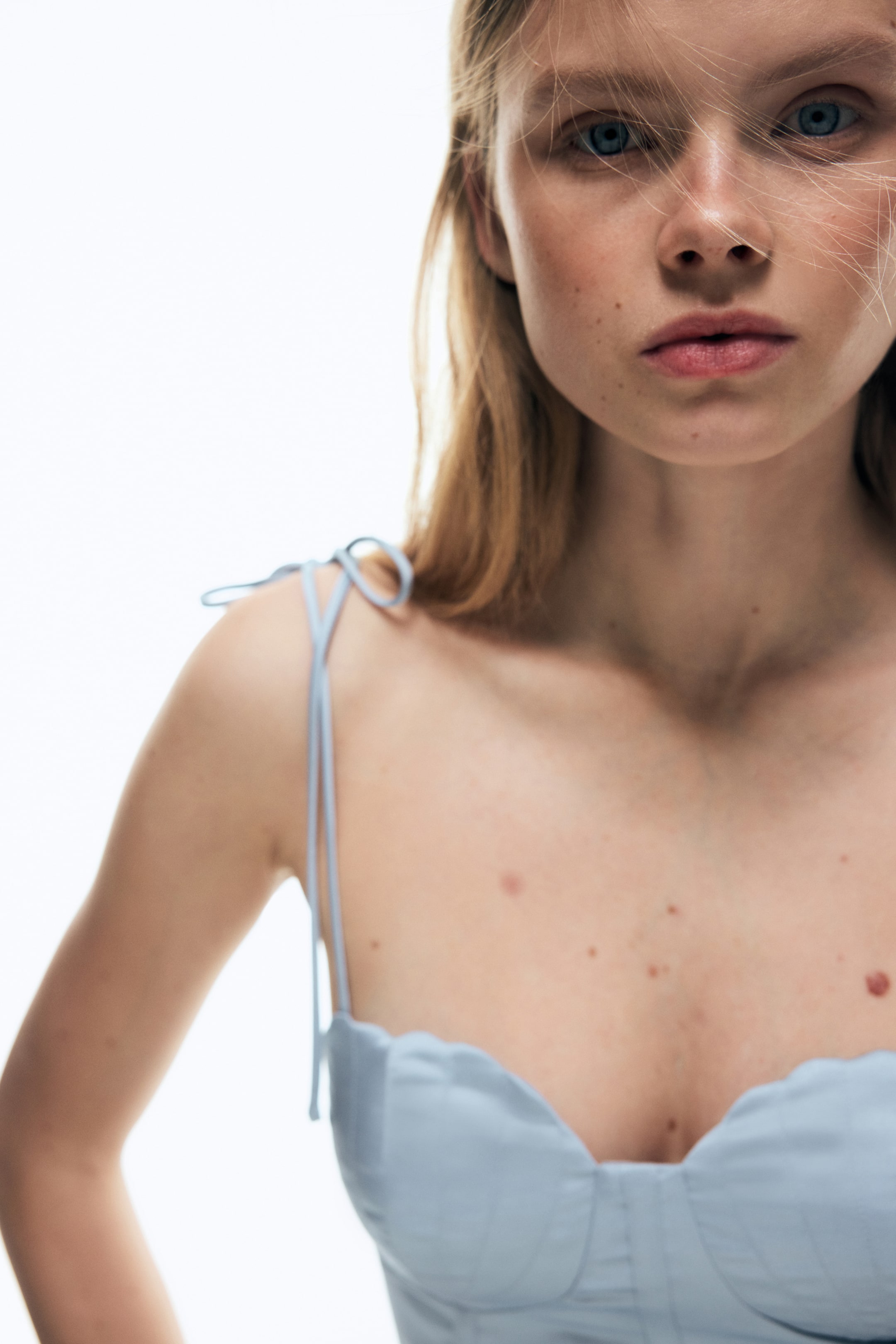 View larger image: A light blue top featuring thin spaghetti straps tied into bows at the shoulders, a scalloped sweetheart neckline, and a structured bust with visible seam detailing.