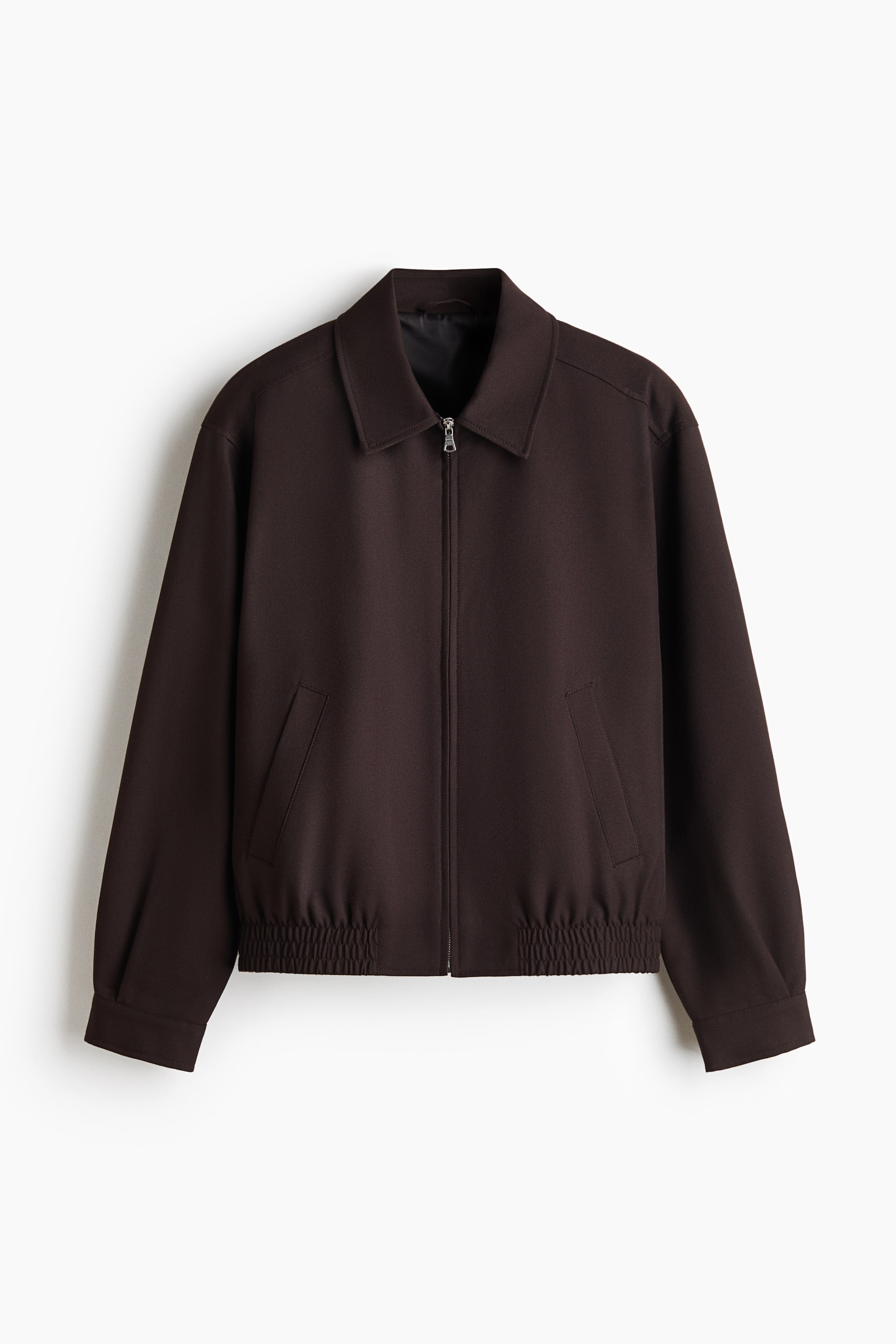 View larger image: A dark brown jacket is facing the front, showcasing a classic point collar, a full-length silver zipper closure, and two angled welt side pockets. The design features long sleeves with simple cuffs and an elasticated, gathered hem at the waist.