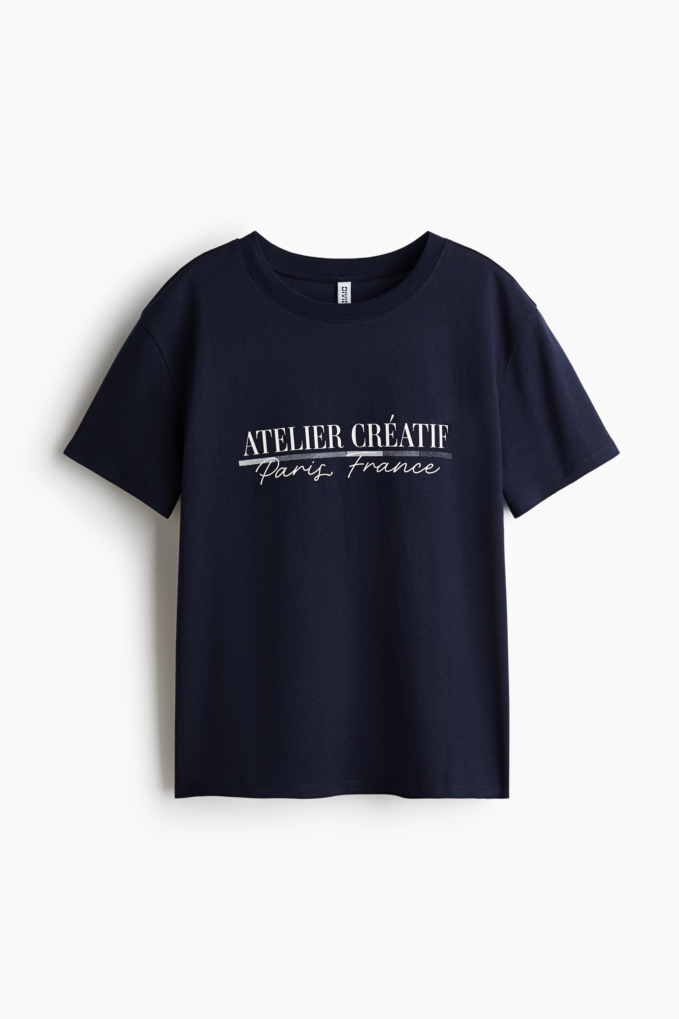 Má»t chiáº¿c Ã¡o thun mÃ u xanh navy, dÃ¡ng rá»ng, lÃ m tá»« cotton jersey má»m máº¡i Äang ÄÆ°á»£c hiá»n thá» á» gÃ³c chá»¥p chÃ­nh diá»n, vá»i cá» trÃ²n viá»n bo gÃ¢n, vai trá» vÃ  há»a tiáº¿t chá»¯ in mÃ u tráº¯ng ghi "ATELIER CRï¿½ATIF Paris France" ngang ngá»±c. Ão rá»§ nháº¹ theo dÃ¡ng cÆ¡ thá» vÃ  ÄÆ°á»£c phá»i vá»i pháº§n gáº¥u Ã¡o hÆ¡i kÃ©o cao má»t bÃªn bÃªn trÃªn quáº§n short denim tráº¯ng.