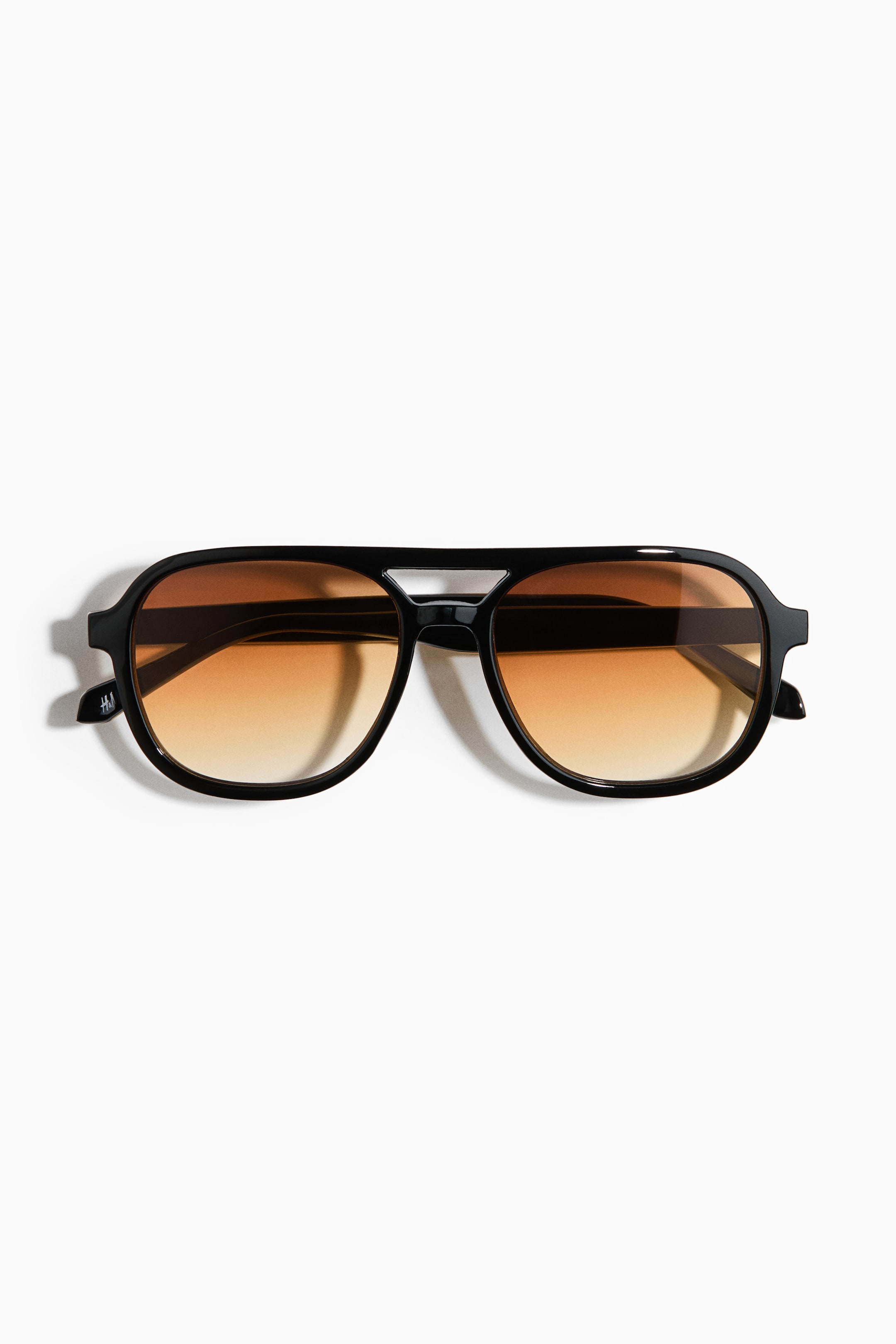 View larger image: Black aviator-style sunglasses are lying flat, facing forward, displaying a double bridge and brown gradient lenses.