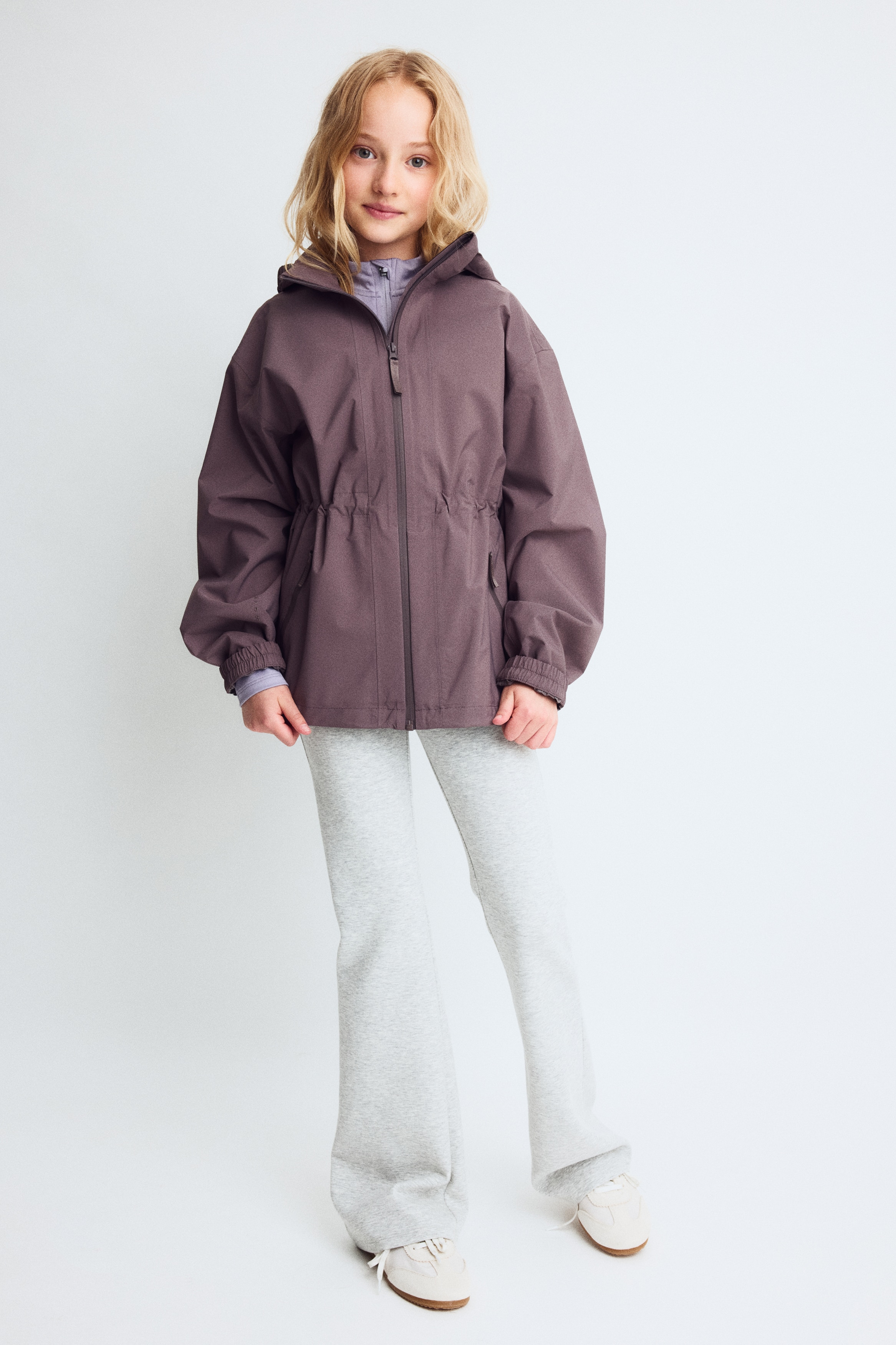 A rain jacket with StormMove? is showcasing its front view in a muted purple colour. It features a full-length central zip, an attached hood, two zippered front pockets, elasticated cuffs, and an elasticated hem.