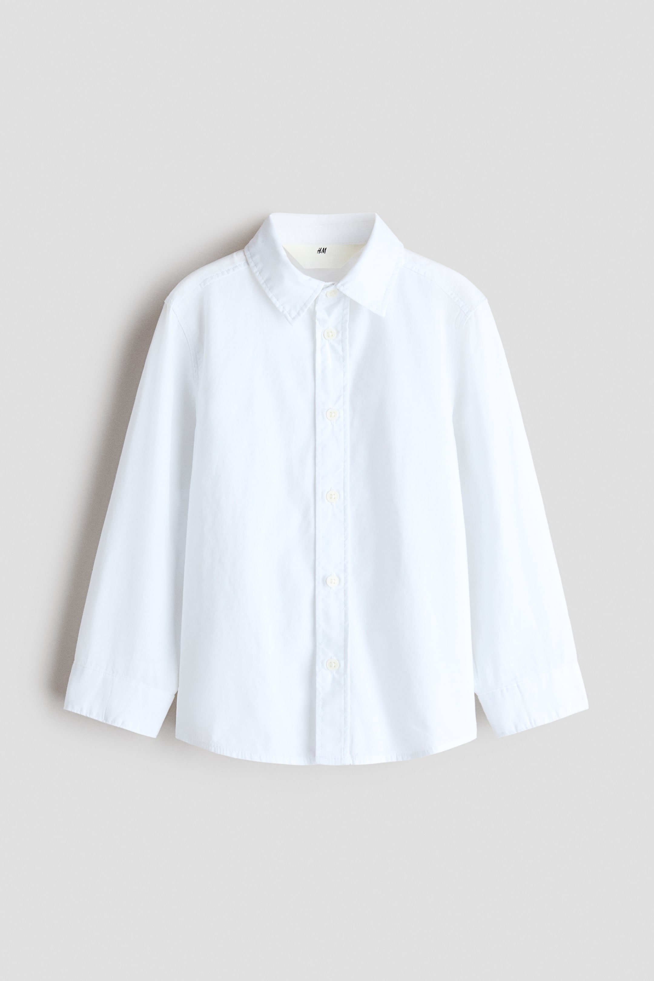 Visualizza l'immagine ingrandita: Una camicia bianca a maniche lunghe in tessuto di cotone è mostrata frontalmente, con colletto a punta, abbottonatura frontale e maniche lunghe con polsini. La camicia presenta un orlo leggermente arrotondato.