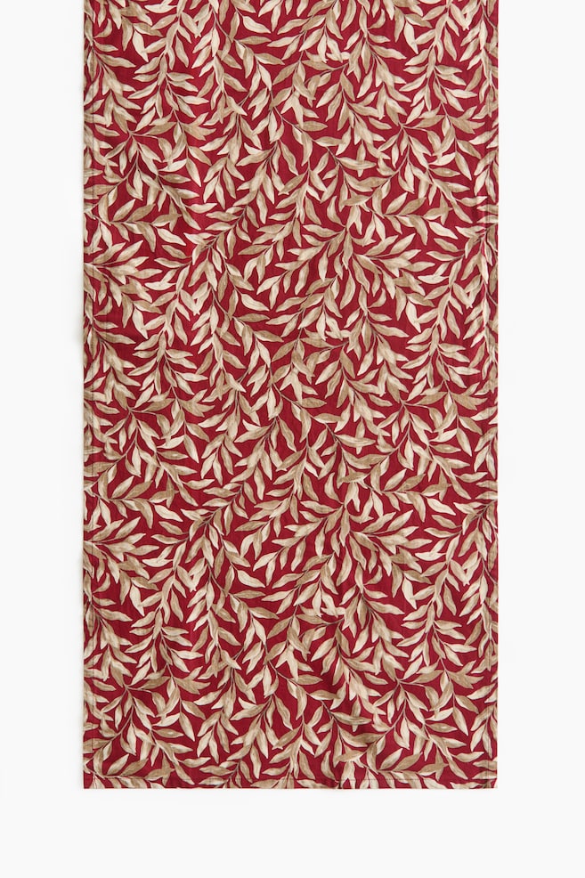 Un chemin de table rectangulaire en tissu est suspendu verticalement, mettant en valeur un motif botanique intÃ©gral de feuilles beige et crÃ¨me sur un fond rouge profond. Cette vue de face souligne le motif de vigne rÃ©pÃ©tÃ© ainsi que les bords nets et finis. - 1