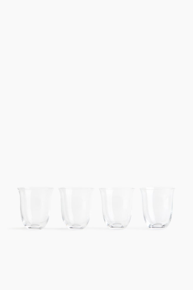 Four clear glass tumblers are standing in a horizontal row facing forwards, showcasing their delicate, thin-walled construction. Each tumbler curves gently outwards from a rounded base to a slightly flared rim. - 1