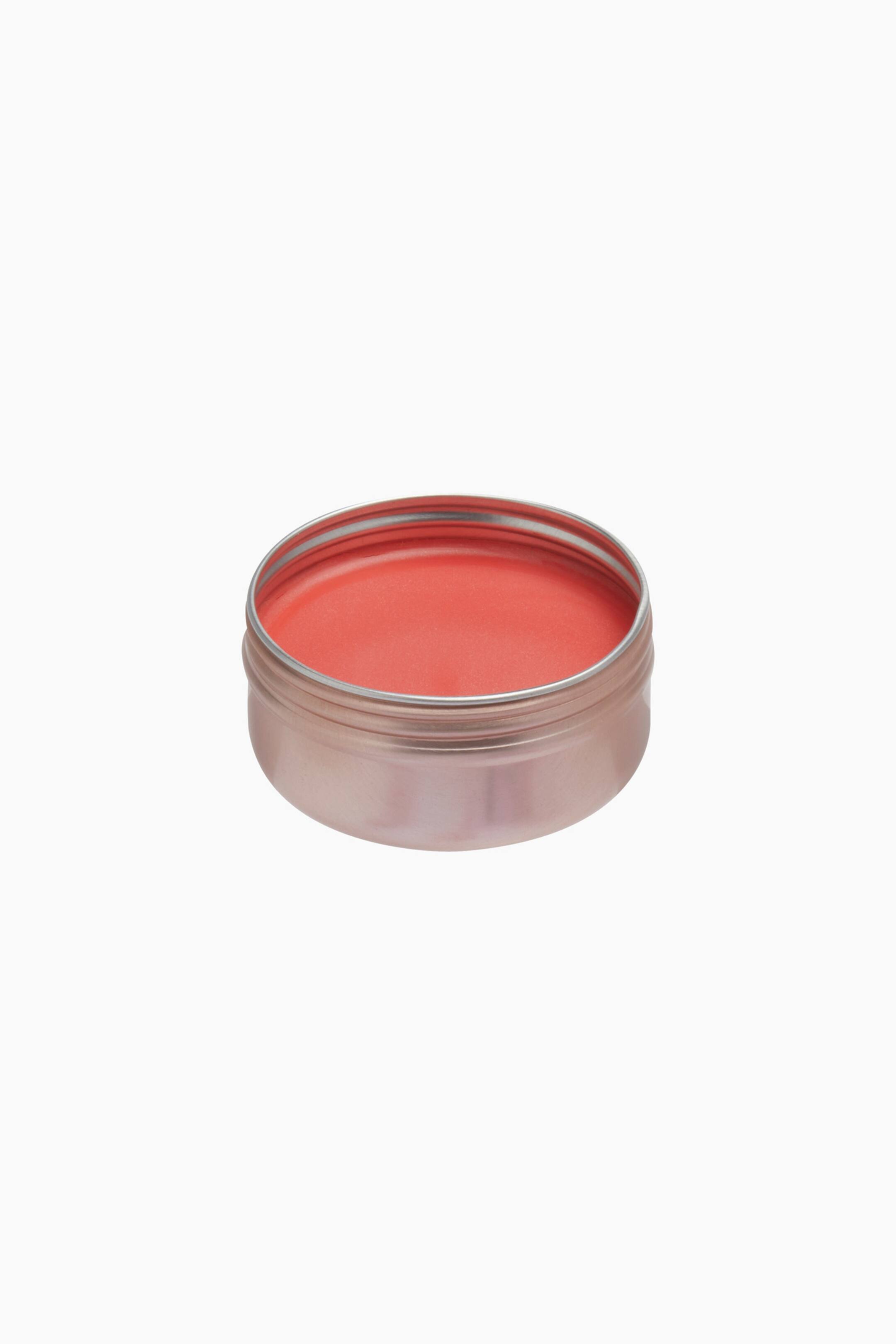 Größeres Bild ansehen: Eine runde, offene Metalldose in Roségold-Optik hält einen glatten, korallrosa Balm; sie ist aus einer hohen Drei-Viertel-Perspektive aufgenommen. Der feste Balm zeigt eine saubere, makellose Oberfläche und ist bis knapp unter den inneren Rand des Behälters gefüllt.