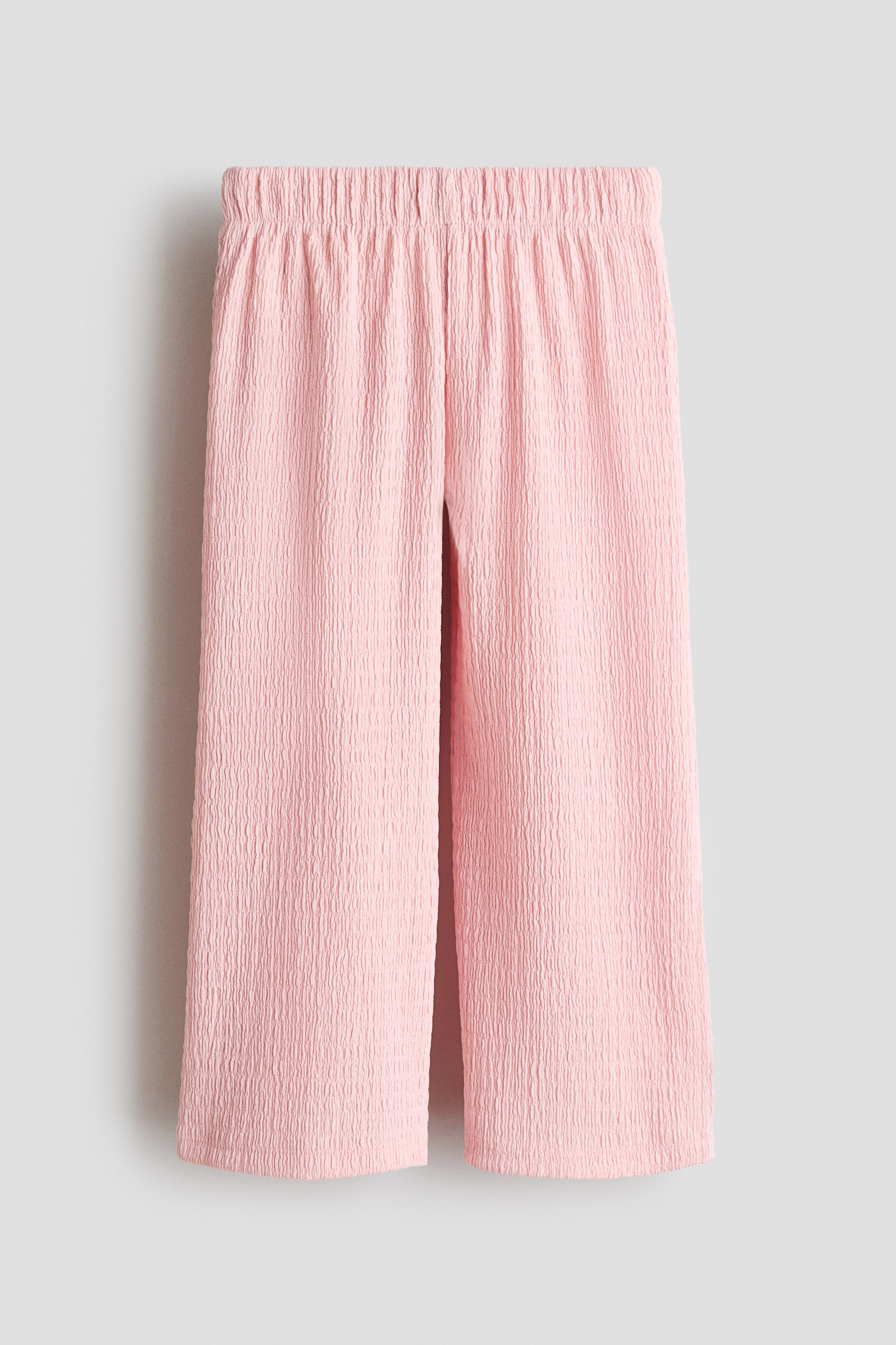 Größeres Bild ansehen: Die hellrosa Hose zeichnet sich durch eine geknitterte Jersey-Textur, einen elastischen Bund und weite Beine aus, präsentiert von vorne.
