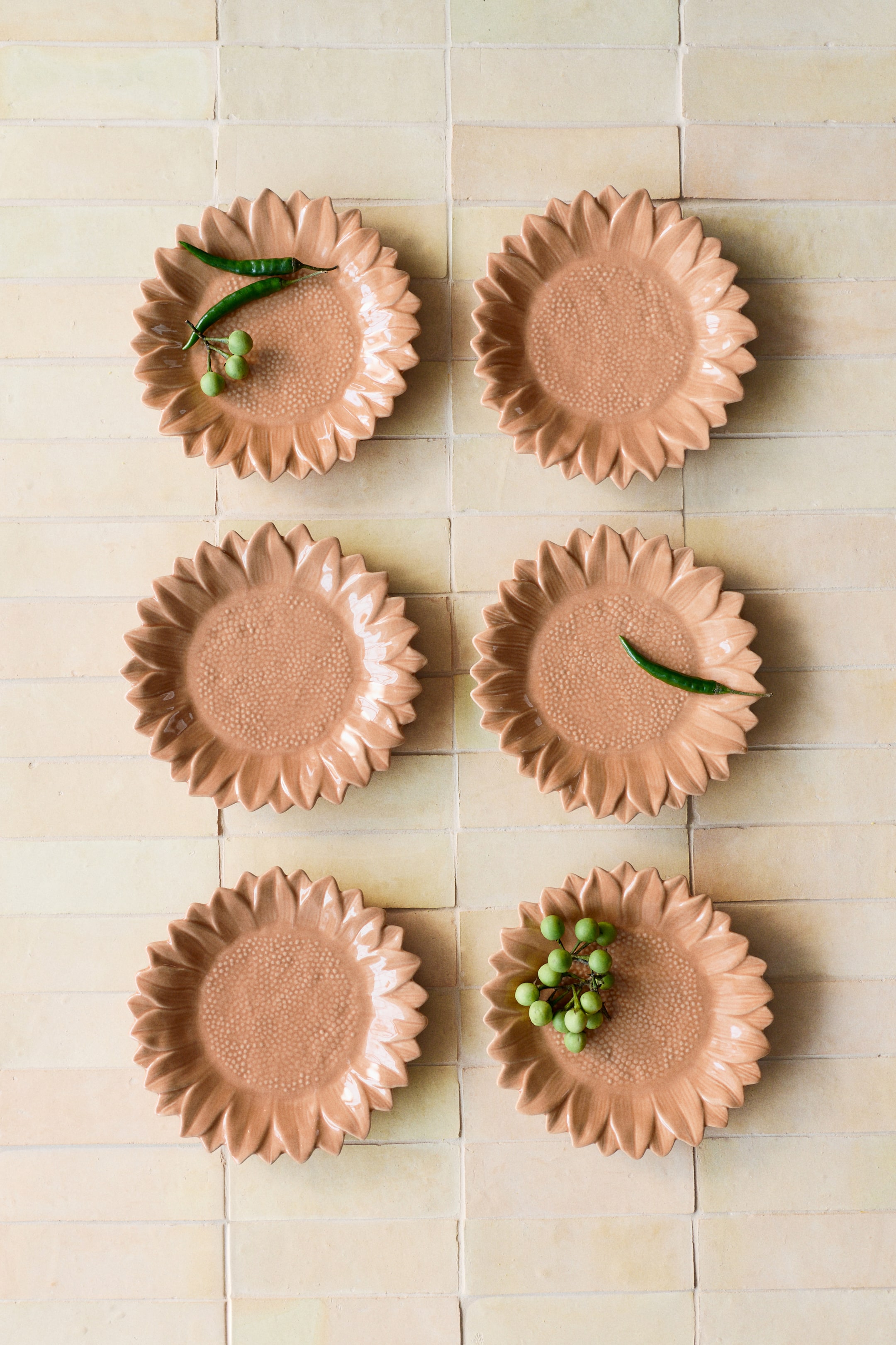 View larger image: The mid-sized plate, crafted from glazed stoneware, is designed to resemble a sunflower in full bloom, showcasing a light terracotta hue. The front features a central dotted texture, while sculpted petals form the outer rim. Some plates also display small green peppers and berries.