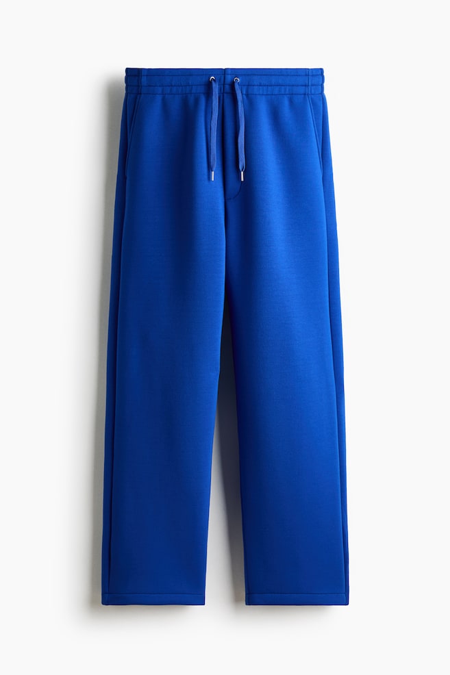 Royal blue joggers, made from scuba fabric, are presenting from the front, featuring a relaxed, straight-leg fit, an elasticated drawstring waist with silver-tipped drawstrings, a faux fly seam, and diagonal side pockets. - 1