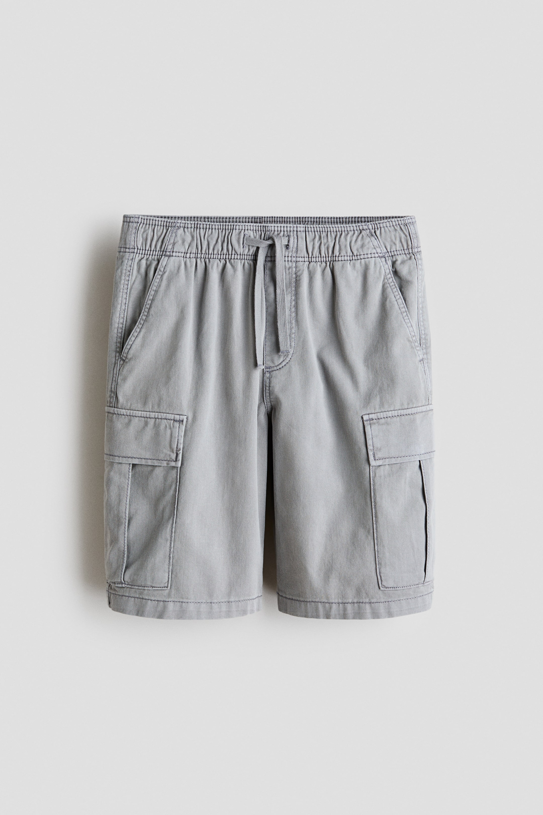 Größeres Bild anzeigen: Knie-lange graue Baumwoll-Twill-Shorts in Vorderansicht, mit einem elastischen Kordelzugbund, einem Fake-Reißverschluss, diagonalen Seitentaschen und Klappentaschen an jedem Oberschenkel.