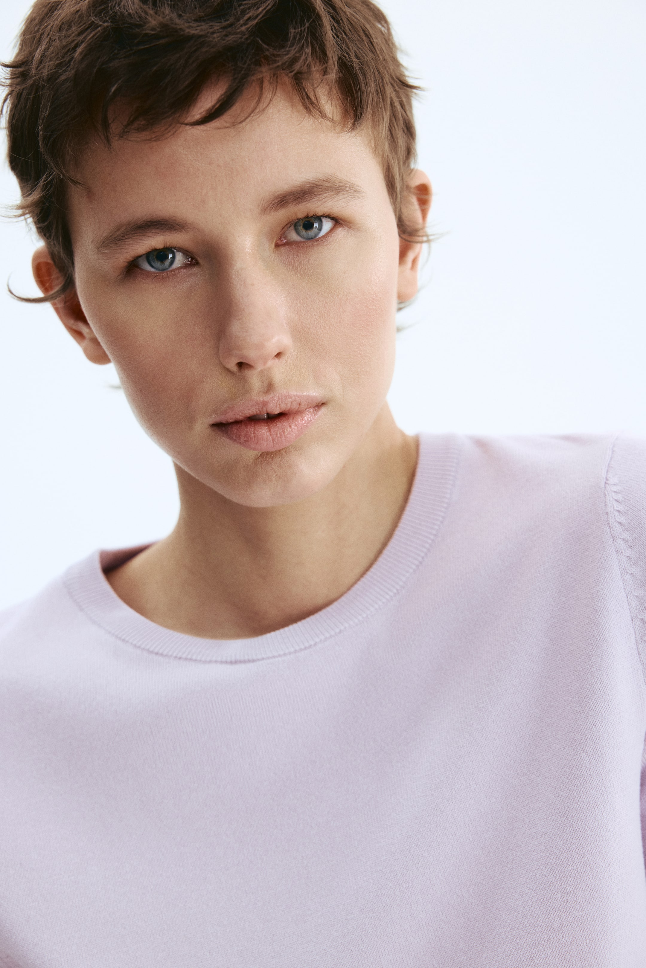 Voir une image plus grande: Un haut à manches courtes de couleur mauve clair en maille fine est porté par le mannequin, avec des côtes autour de l'encolure. Le mannequin regarde vers l'avant.