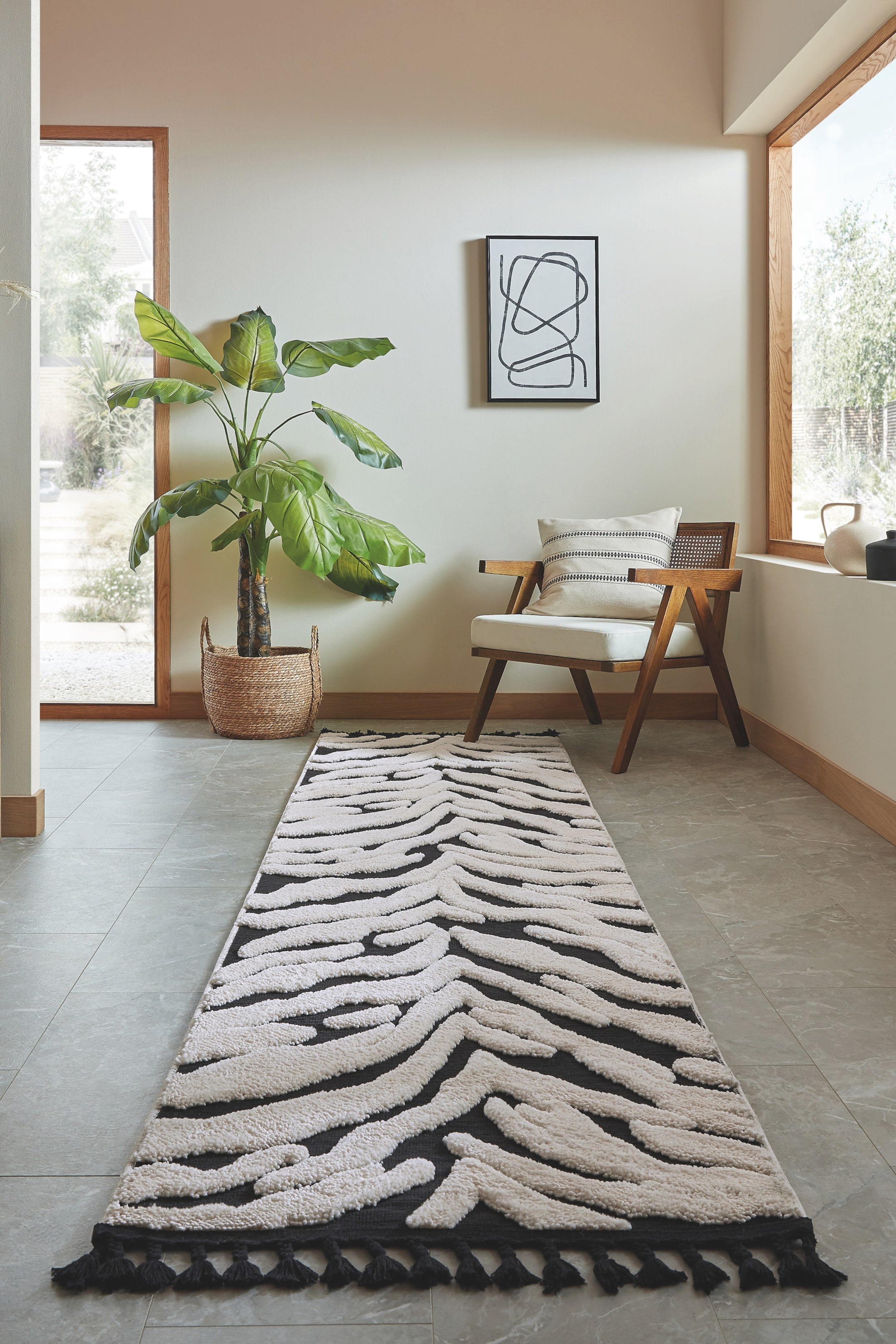 Visualizza immagine più grande: Un tappeto passatoia presenta un motivo a stampa zebrata in nero e bianco sporco, con sezioni rialzate e strutturate in bianco sporco, e nappine nere visibili a un'estremità. La passatoia si estende in lunghezza lontano dall'osservatore, leggermente inclinata verso destra.