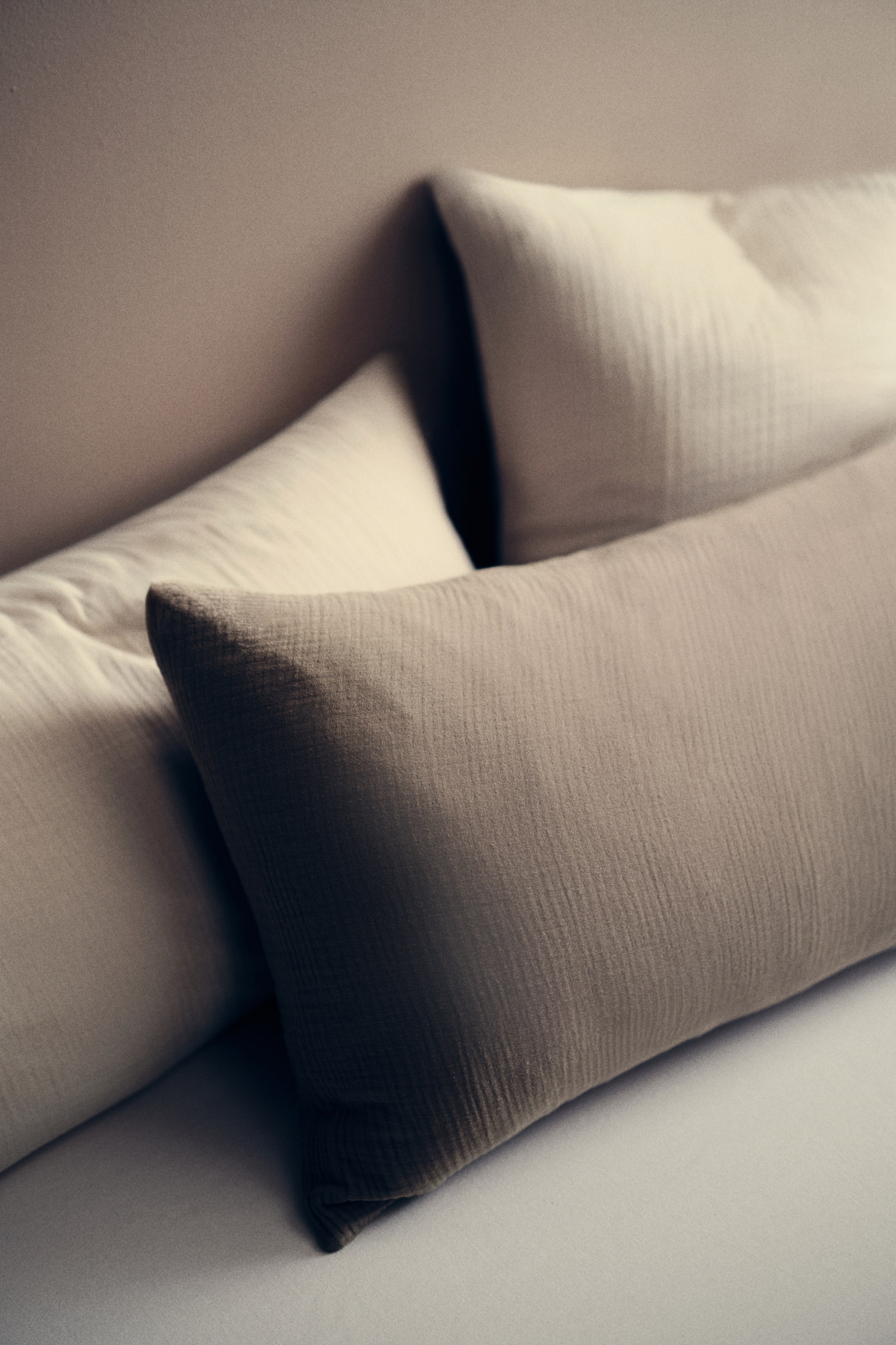 View larger image: A long, rectangular dark beige pillow lies diagonally, showcasing its crinkled fabric texture. It's positioned in front of two lighter beige pillows, which also feature a similar crinkled texture.