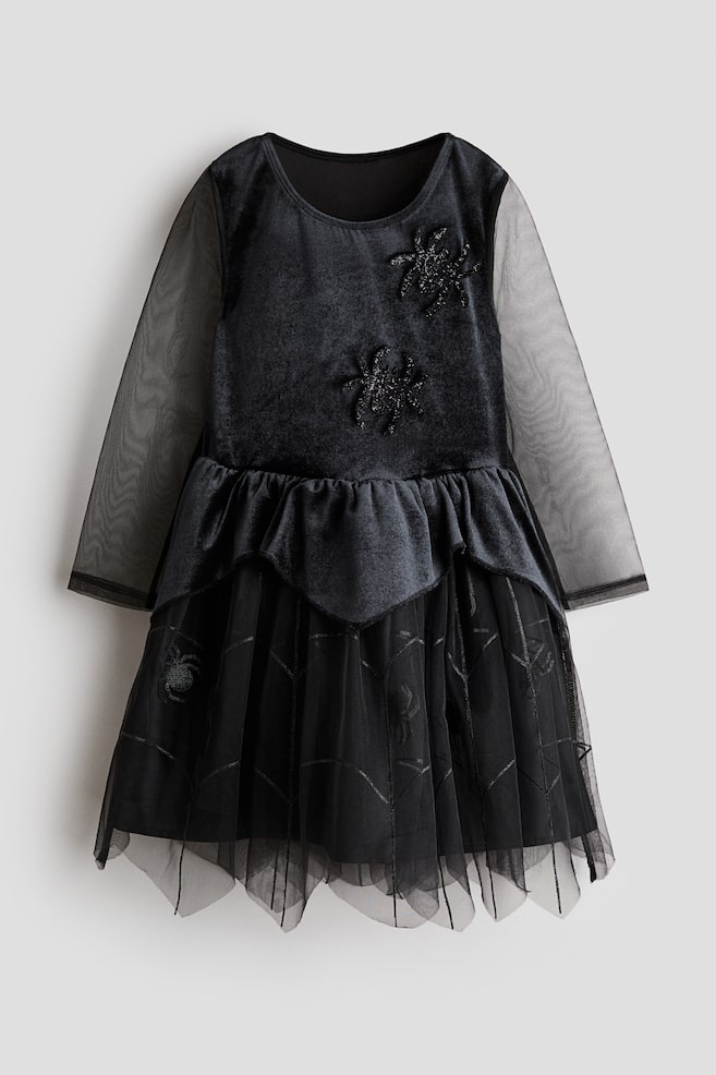 This front-facing view of a children's black dress is showcasing a soft velvet bodice decorated with two glittering spider appliquï¿½s and framed by long, sheer mesh sleeves. The dress is featuring a gathered waist with a pointed velvet peplum overlaying a flared tulle skirt that is displaying subtle spiderweb patterns. - 1