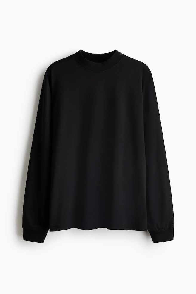A black top in soft cotton and viscose jersey is shown from the front, featuring a ribbed crew neck, low dropped shoulders with slightly forward-facing shoulder seams, and long sleeves with ribbed cuffs. - 1