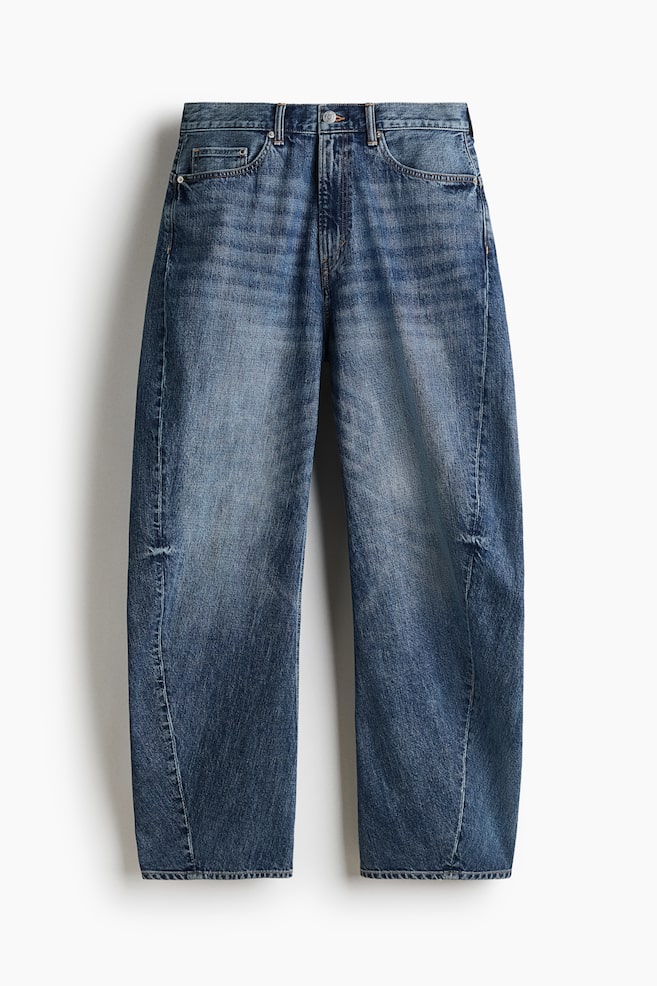 A pair of medium-blue denim barrel-leg jeans is appearing in a front-facing view, showcasing a baggy silhouette with distinctive curved seams that taper slightly at the hem. The jeans are featuring a classic five-pocket design, a regular waist with a button closure, and subtle fading across the thighs. - 1