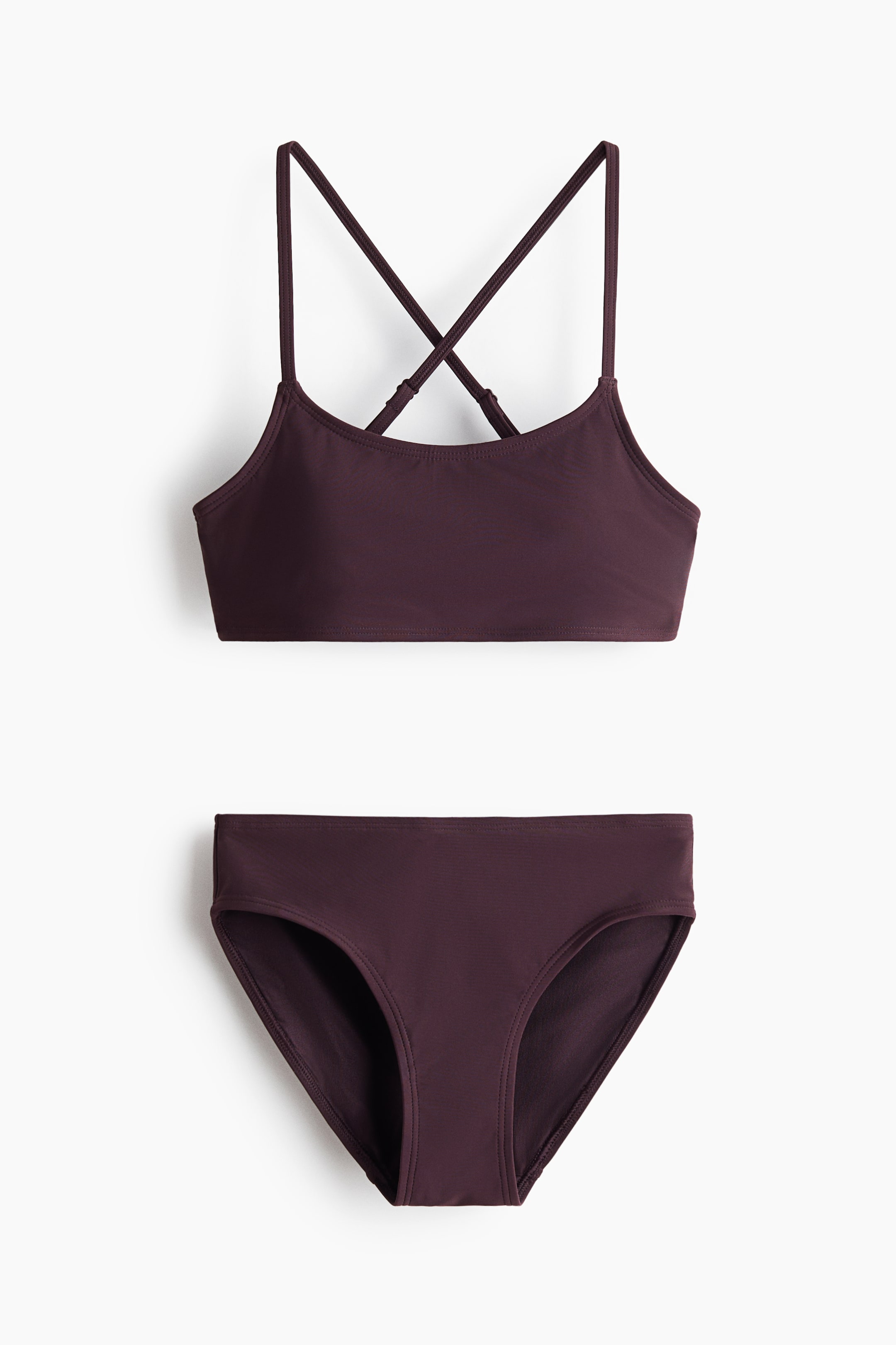 View larger image: A dark plum two-piece swimsuit showcases its bralette-style top and classic bikini bottom from a front-facing angle. The top features thin, adjustable straps that criss-cross at the back.