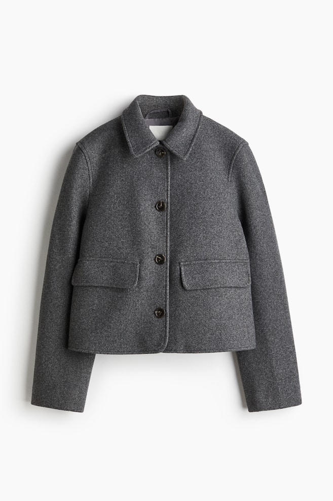 Eine graue, abgeschnittene Jacke ist von vorne zu sehen, mit einem klassischen Spitzkragen, einem Knopfverschluss mit drei dunkelbraunen Knöpfen und zwei großen Pattentaschen mit abgerundeten Klappen an der unteren Vorderseite. - 1