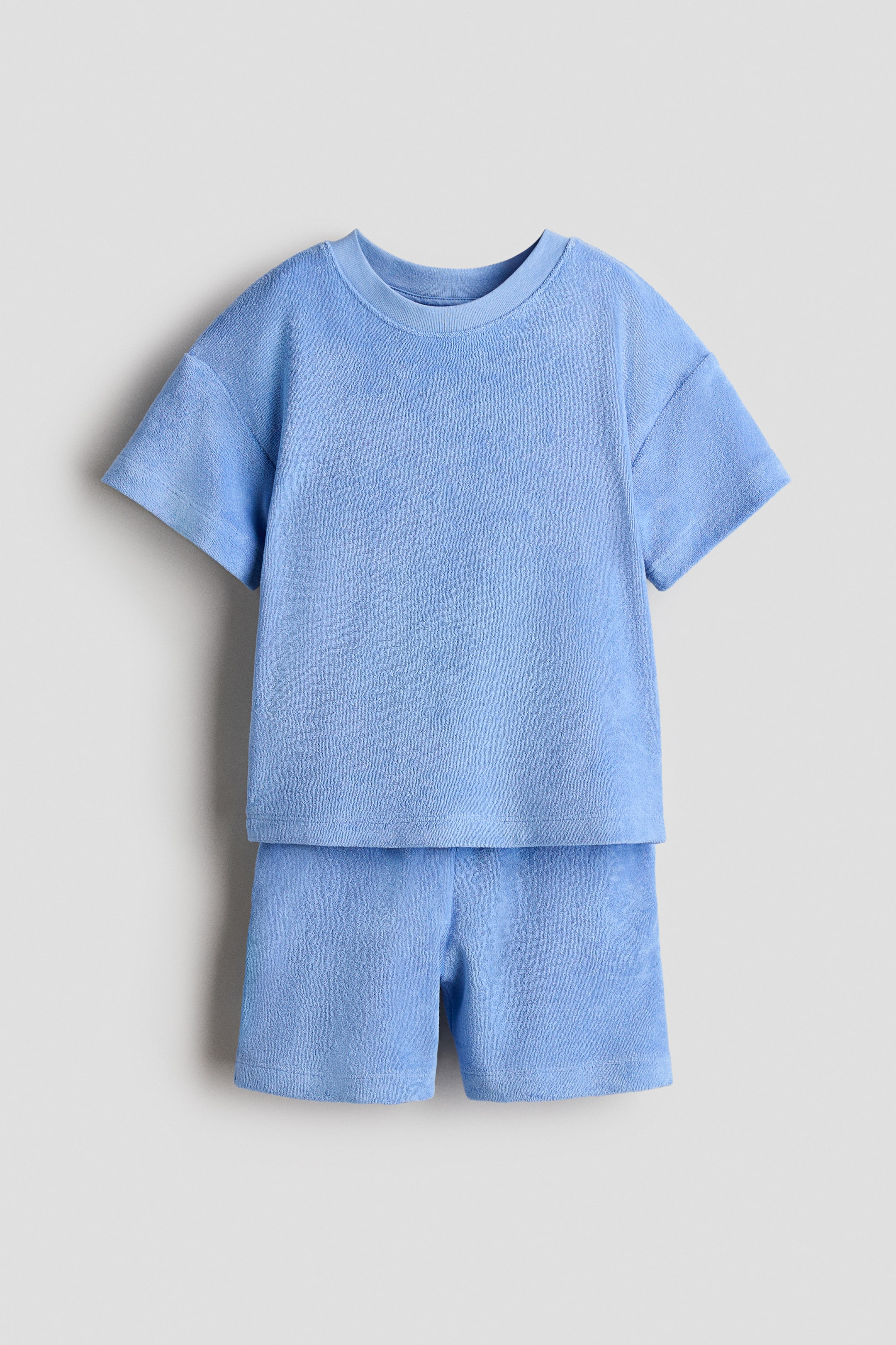 View larger image: "A light blue terry cloth T-shirt and shorts set is displayed from the front. The T-shirt showcases a ribbed crew neck and dropped shoulders, while the matching shorts feature a short length."