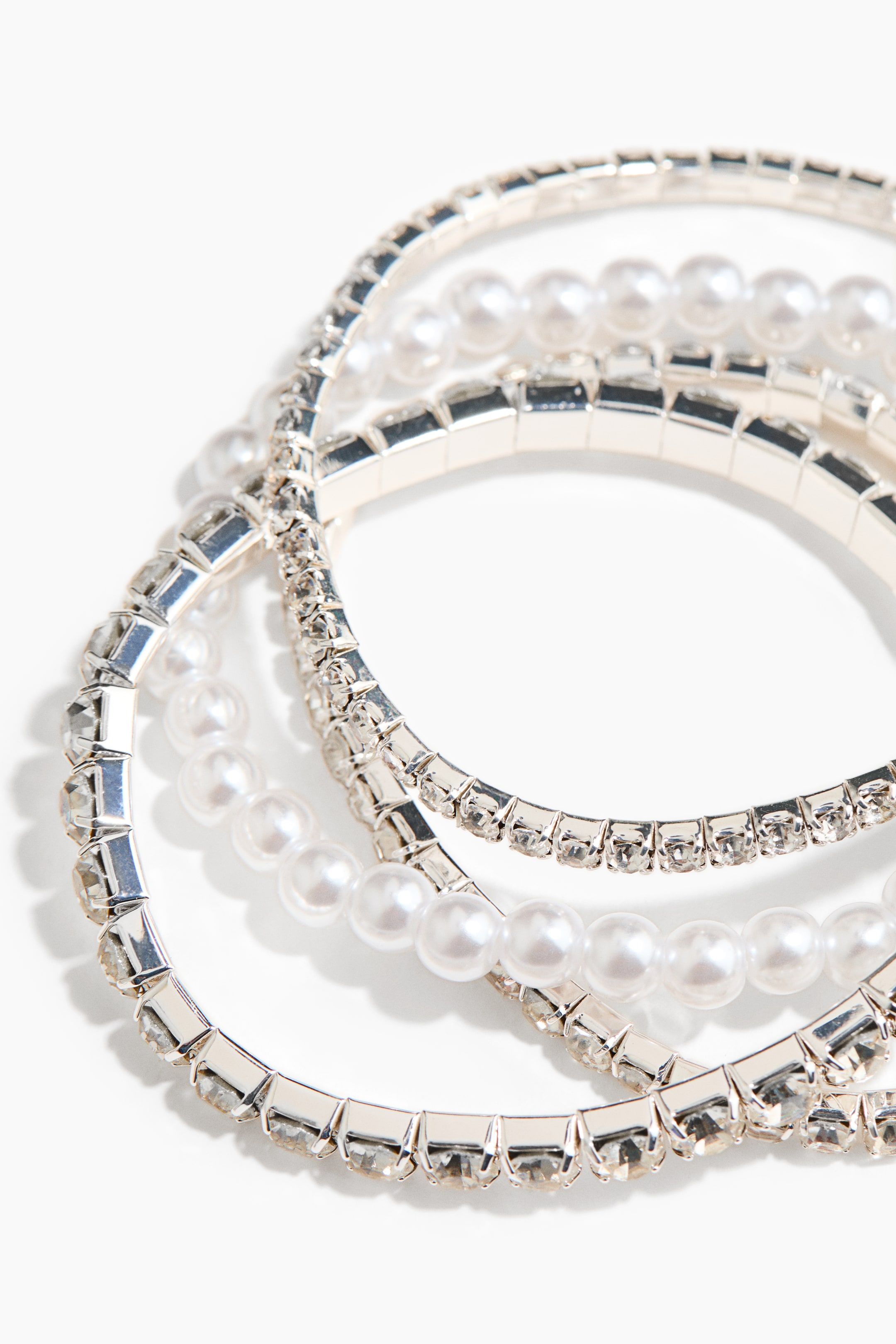 拡大画像を表示: クリアなラインストーンと白いパールの列が交互に配置されたシルバートーンのブレスレットの積み重ねが示されています。いくつかのバンドは重なり合っています。