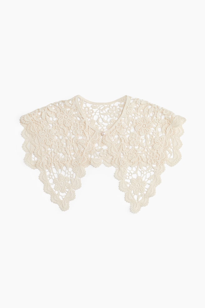 A cream lace collar featuring intricate floral crochet patterns and scalloped edges forming pointed ends at the front. A single pearl button secures its front closure. - 1