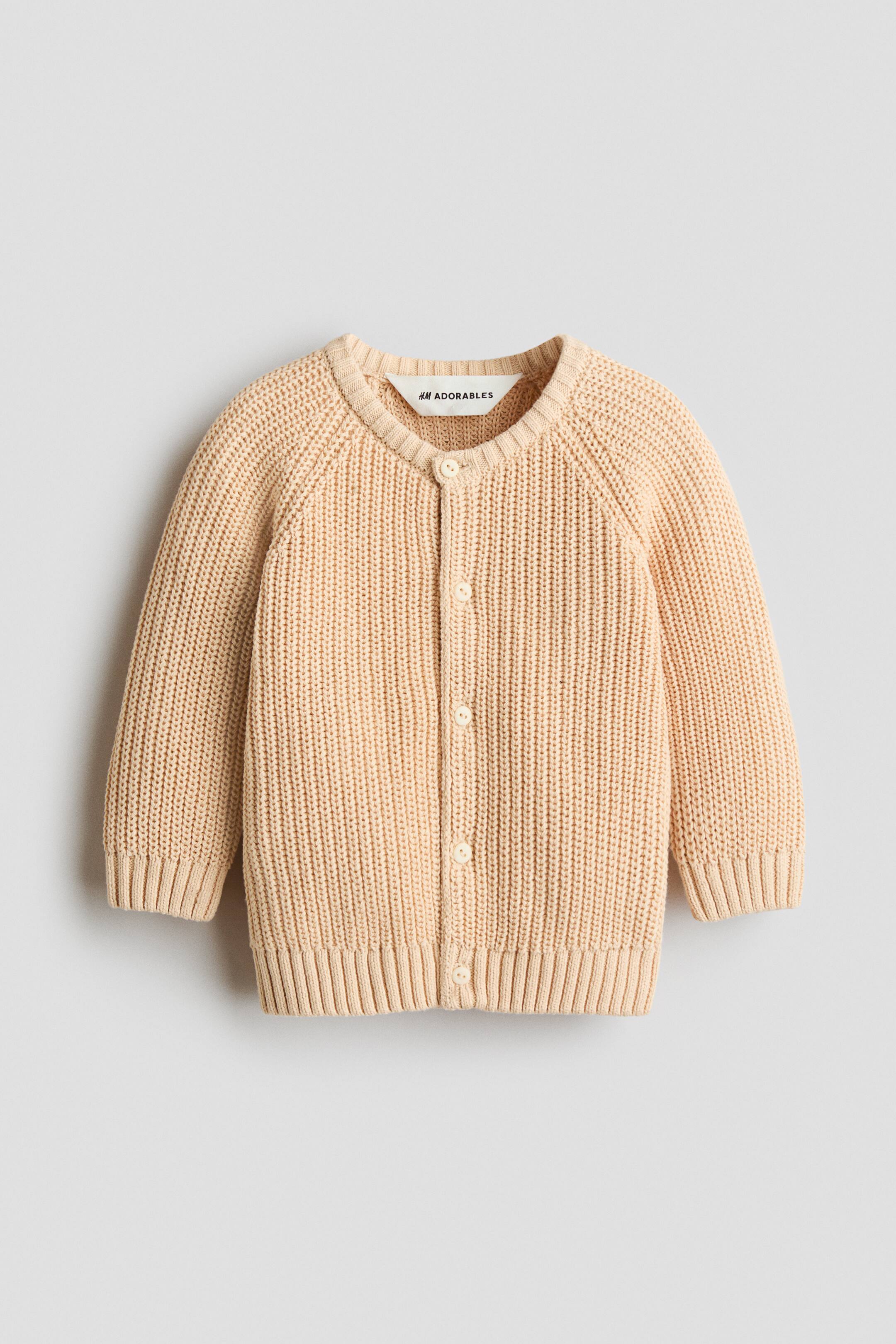 Agrandir l'image: Le cardigan H&M Adorables est présenté de face, mettant en valeur une maille côtelée rose pêche clair. Il présente un col rond bordé de côtes, de longues manches raglan, des boutons clairs sur le devant, ainsi que des finitions côtelées aux poignets et à l’ourlet.