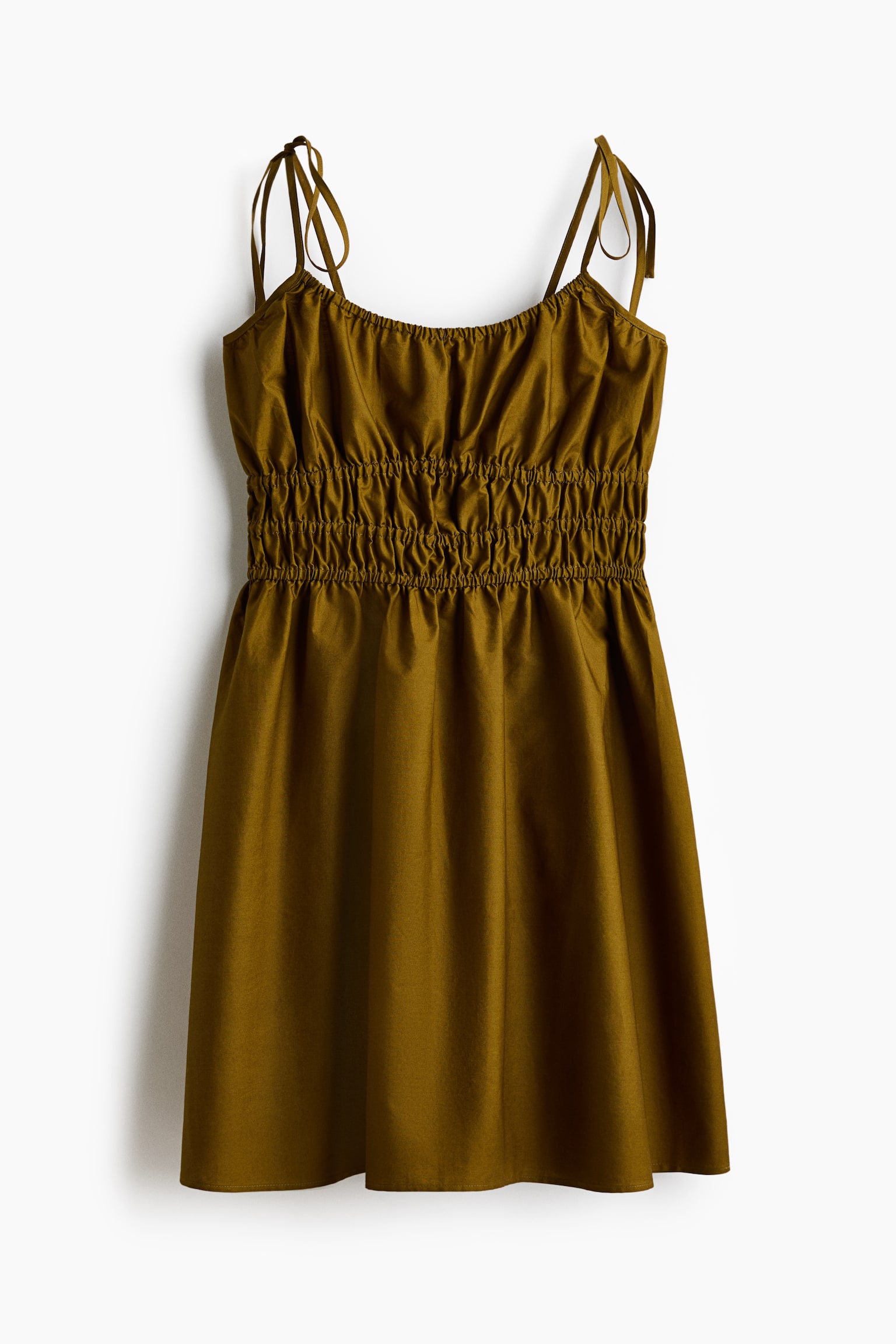 The short dress is displayed front on, featuring a deep, round neckline with covered elastication. It is designed with narrow, tie-top shoulder straps, smocking at the waist, and a flared skirt in an olive green, airy cotton weave. - 1